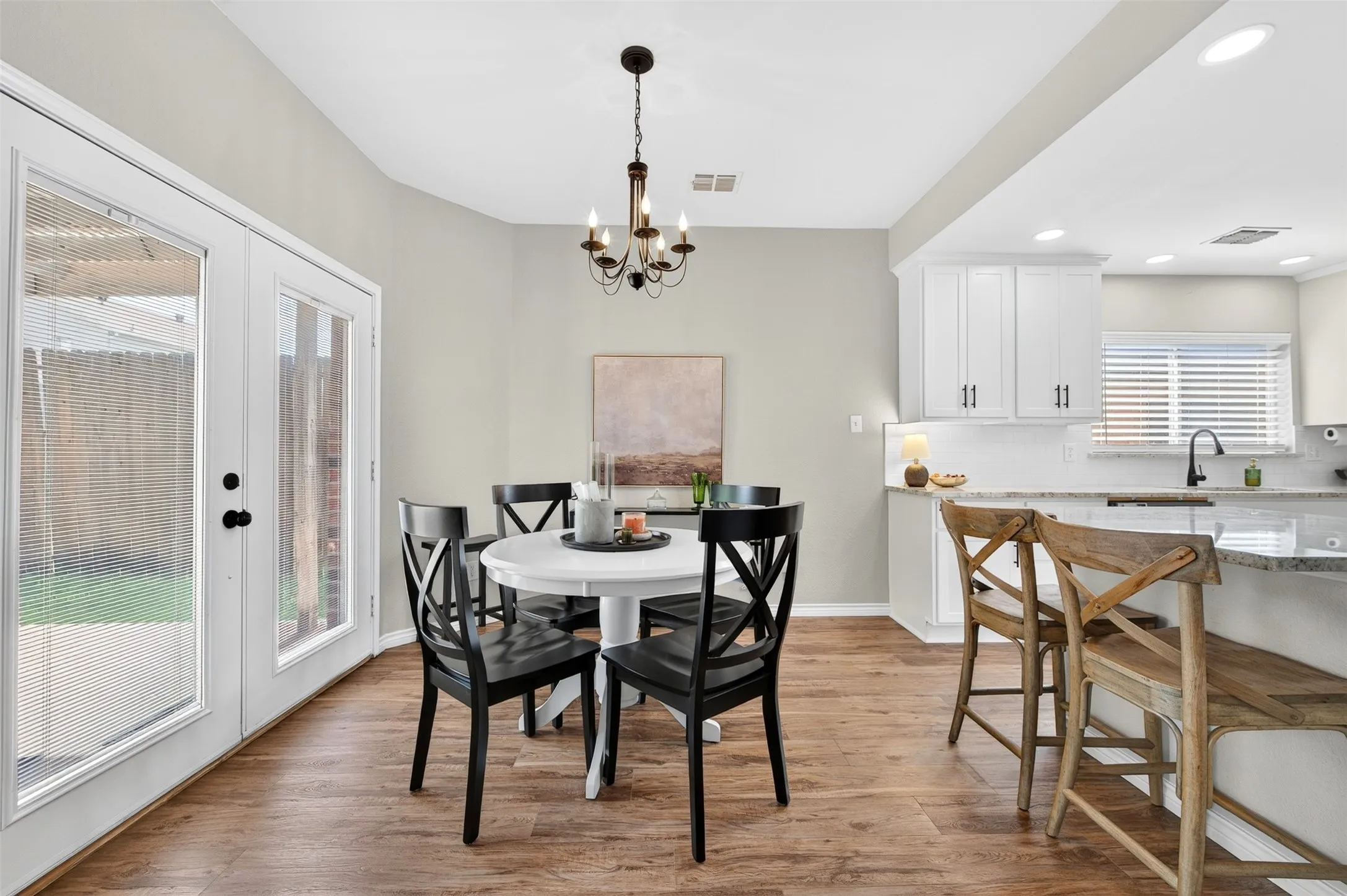 Open-concept dining area featuring wood-finish flooring, a contemporary chandelier, and direct access to the exterior through double-pane glass doors