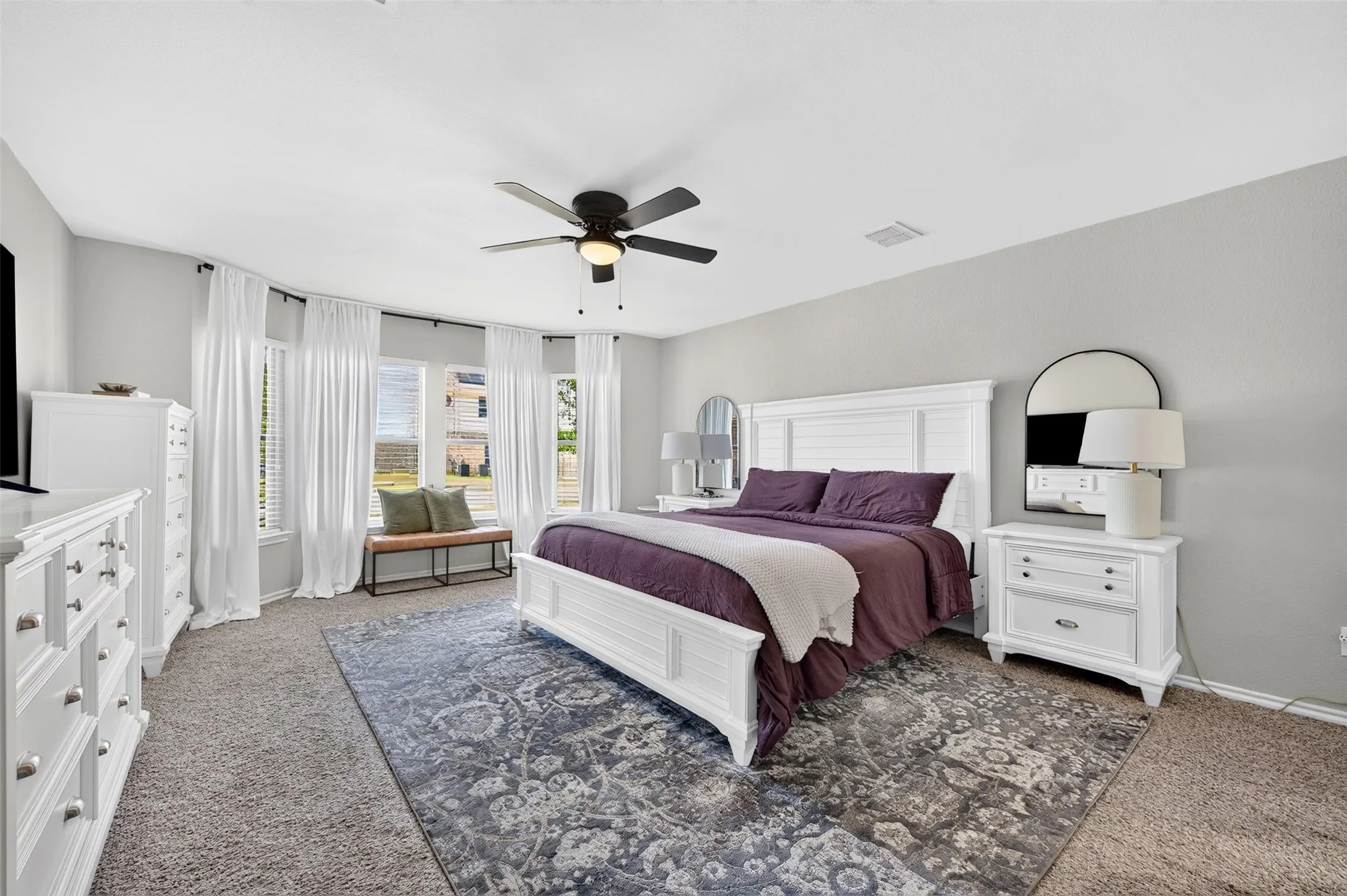 Carpeted room featuring a bay window with window treatments, a ceiling fan with integrated lighting, and light gray wall paint