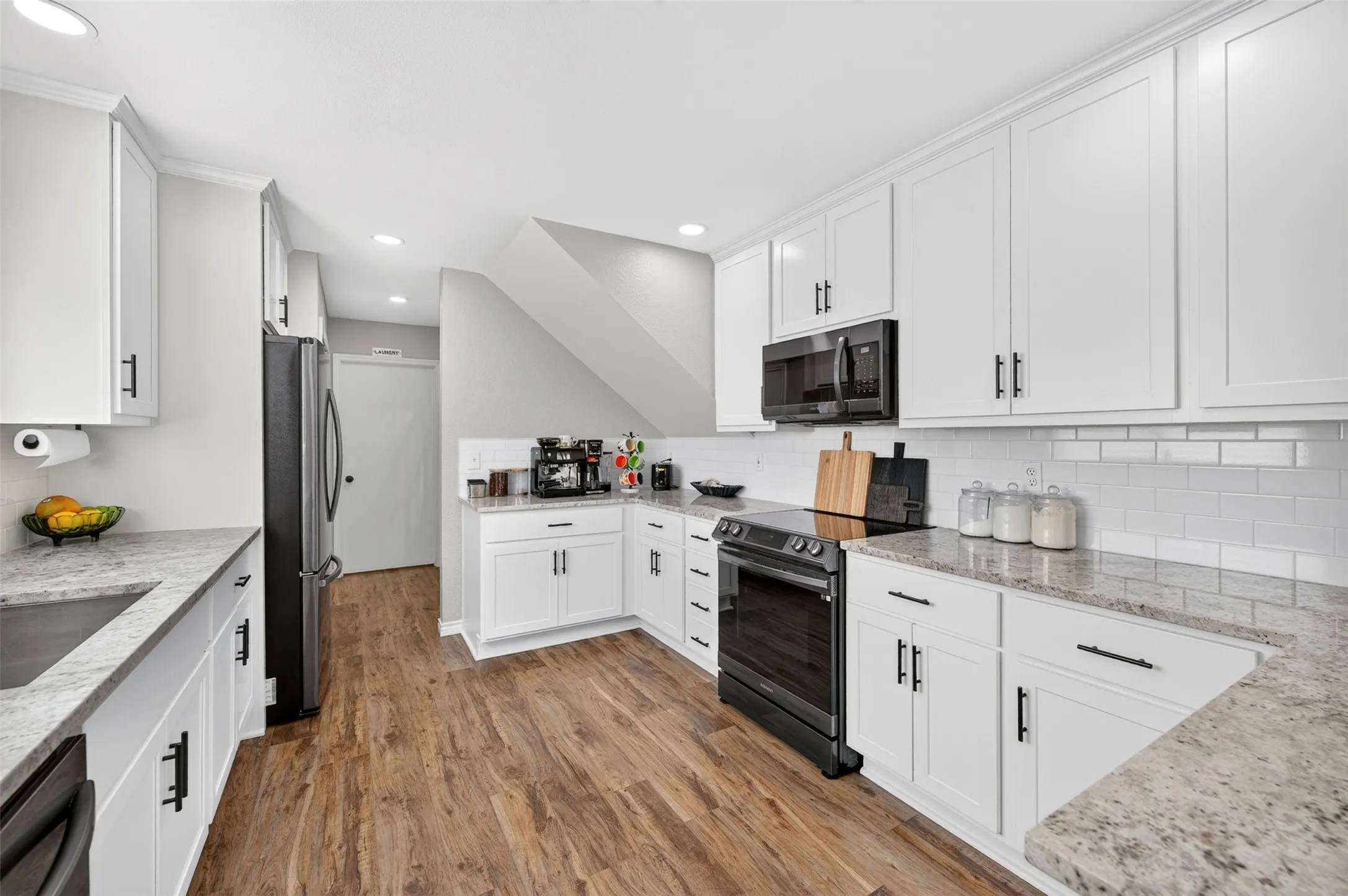 Kitchen featuring white cabinetry, wood-finish flooring, light-toned countertops, a subway tile backsplash, and stainless steel appliances