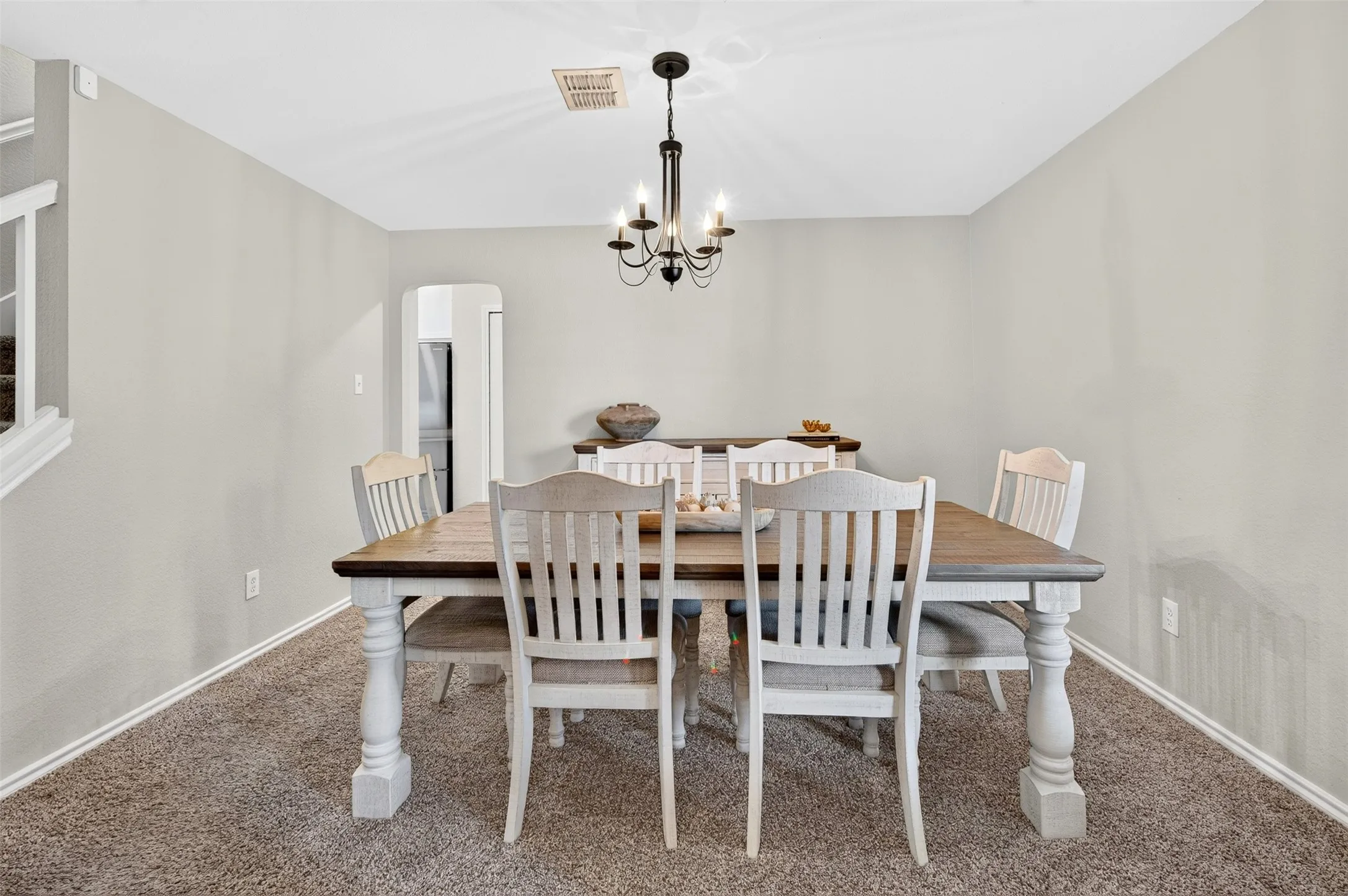 Dining area featuring neutral wall tones, carpet flooring, a black metal chandelier, and a framed archway