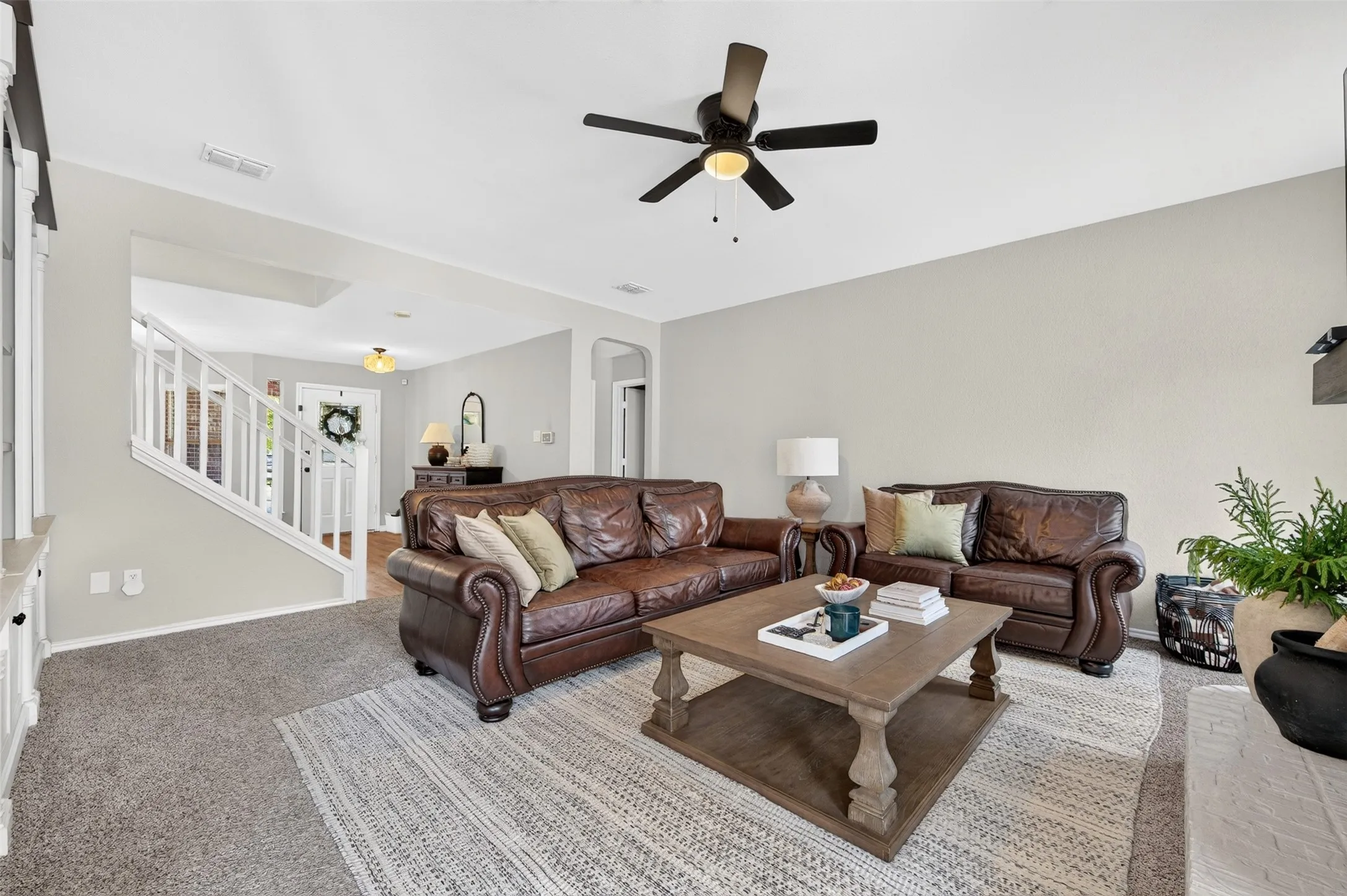 Carpeted living area with light gray walls, a ceiling fan, and a view of the staircase with white railings