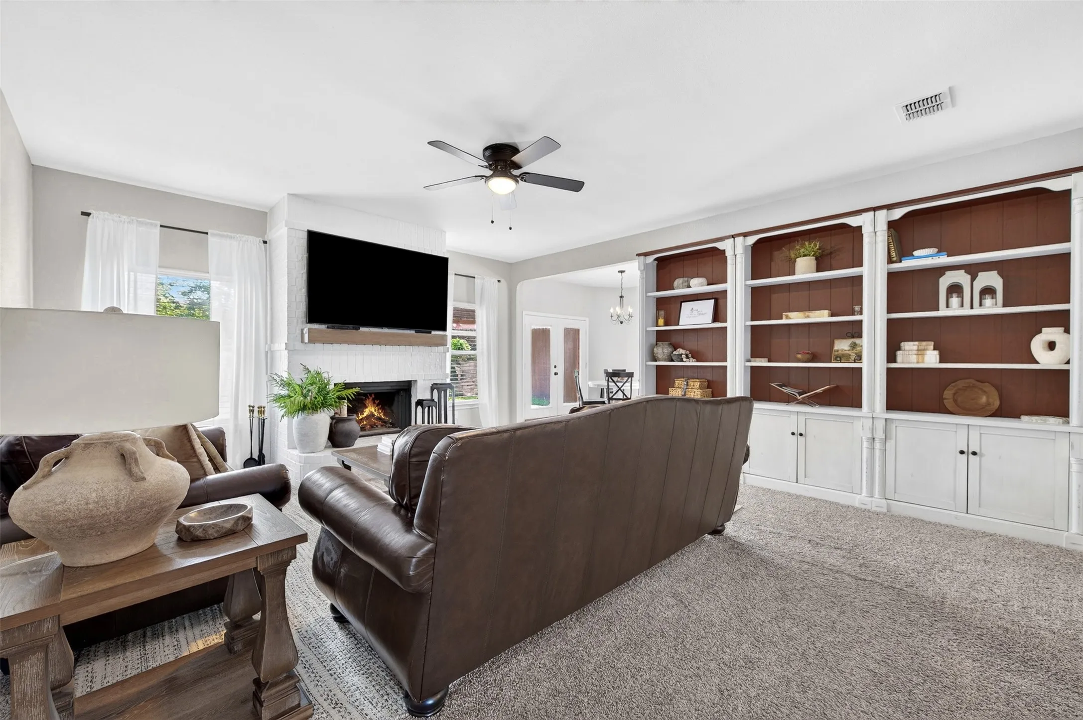 Living area featuring a white brick fireplace with a wood mantel, built-in shelving with lower cabinetry, and carpet flooring