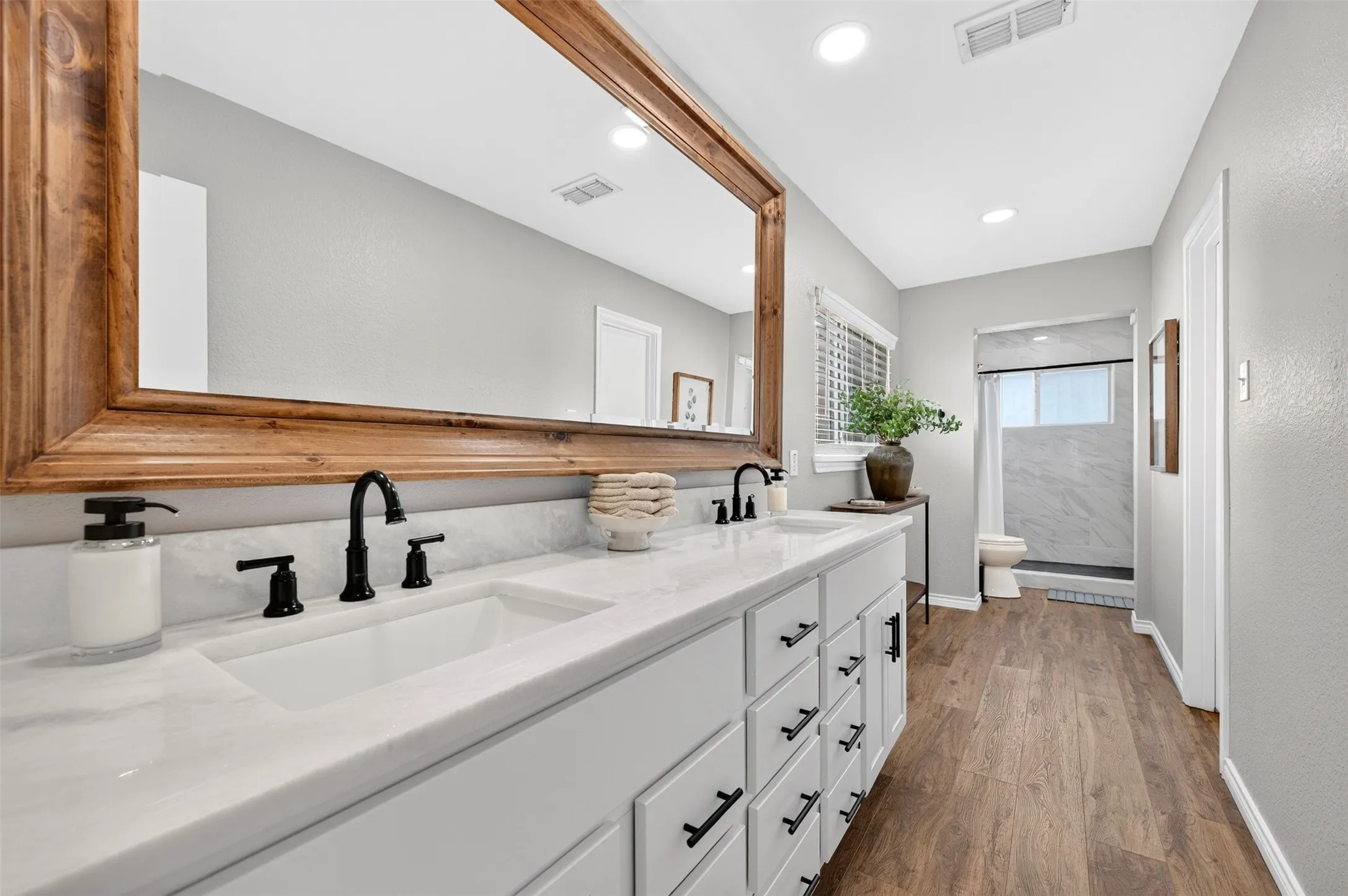 Dual vanity with white cabinetry, matte black hardware, and a large wood-framed mirror