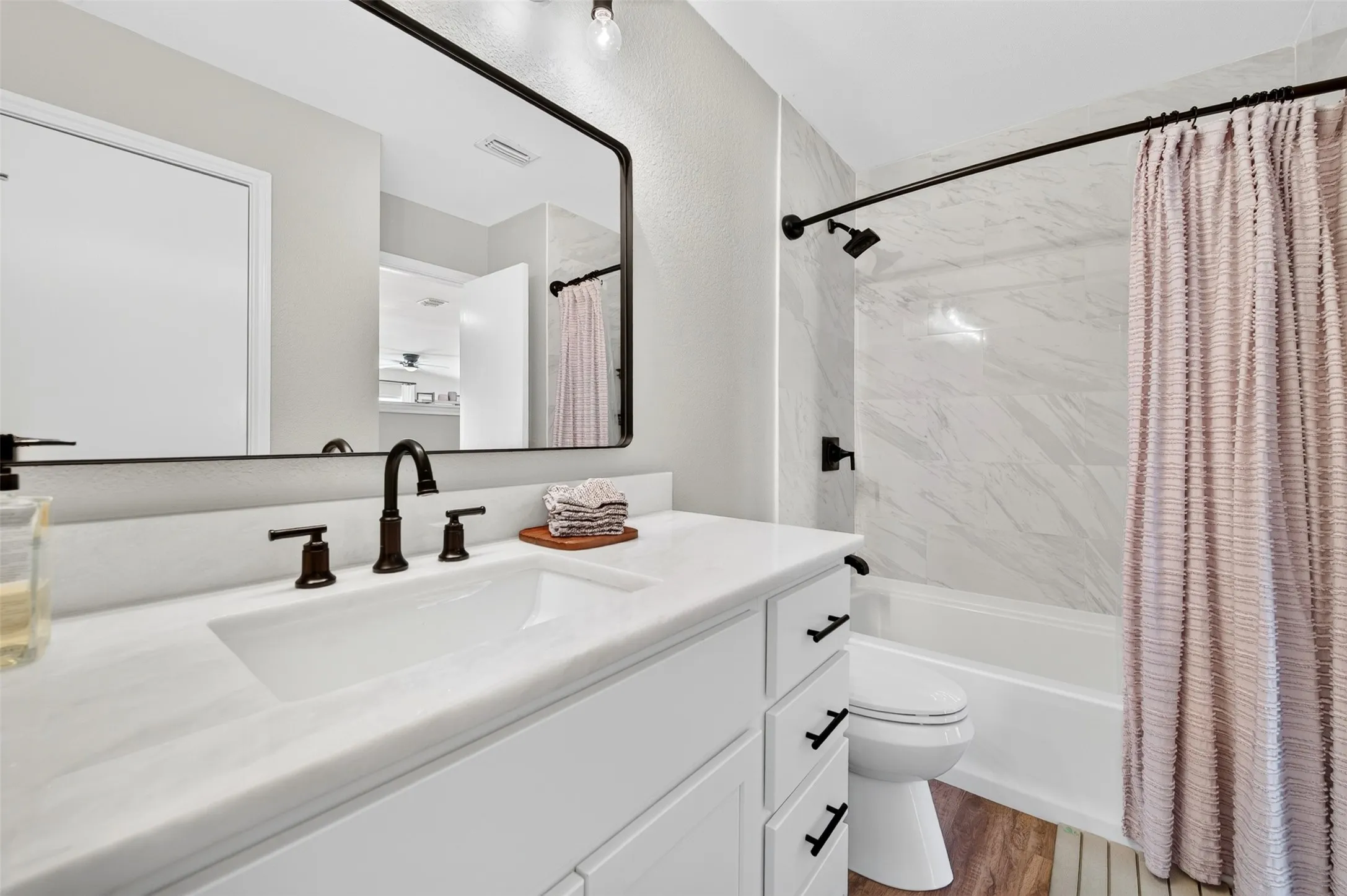 Modern bathroom featuring a white vanity with integrated sink, dark bronze fixtures, and a framed mirror