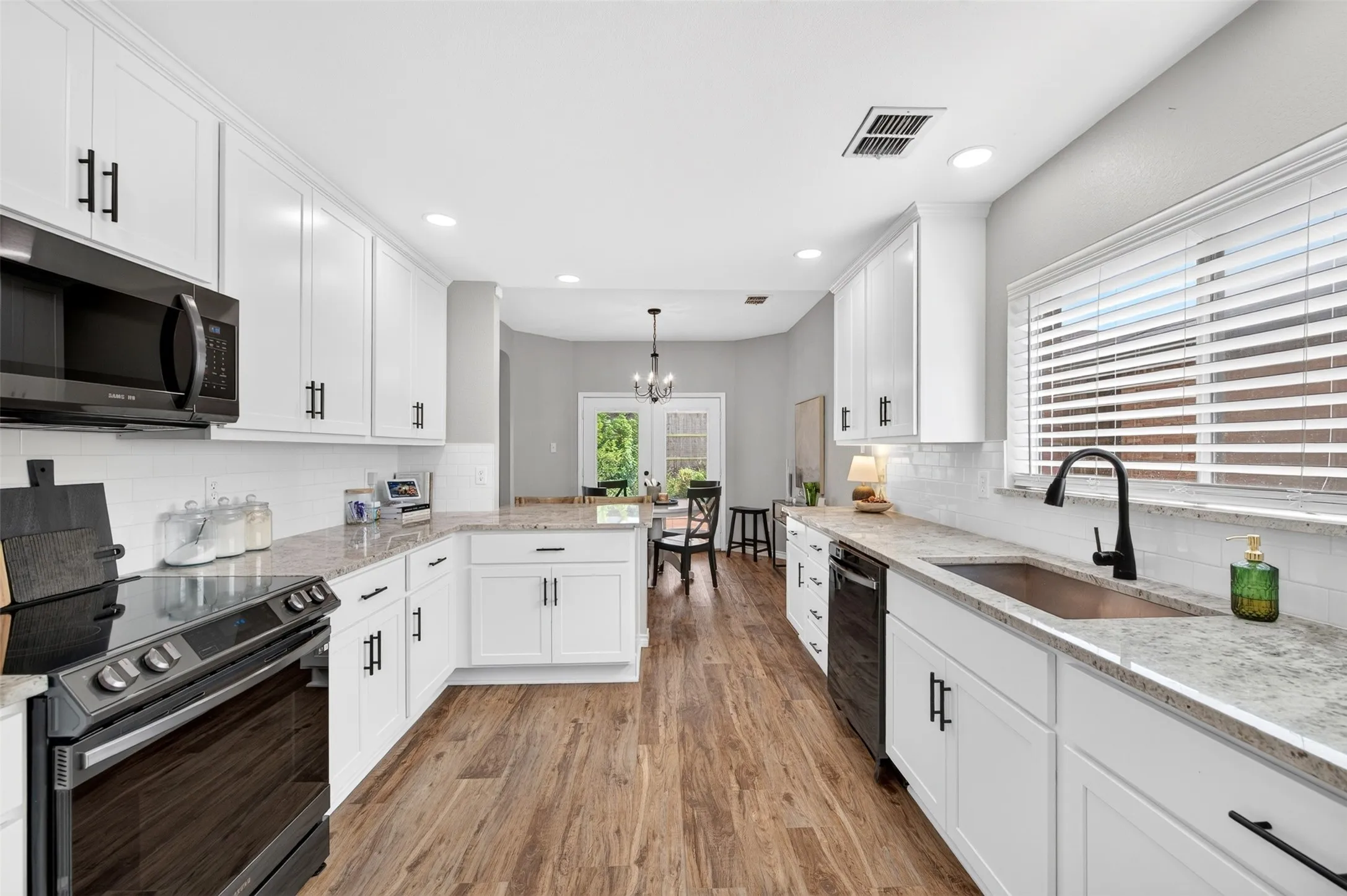 Contemporary kitchen featuring white cabinetry with matte black hardware, light-toned countertops, and wood-finish flooring