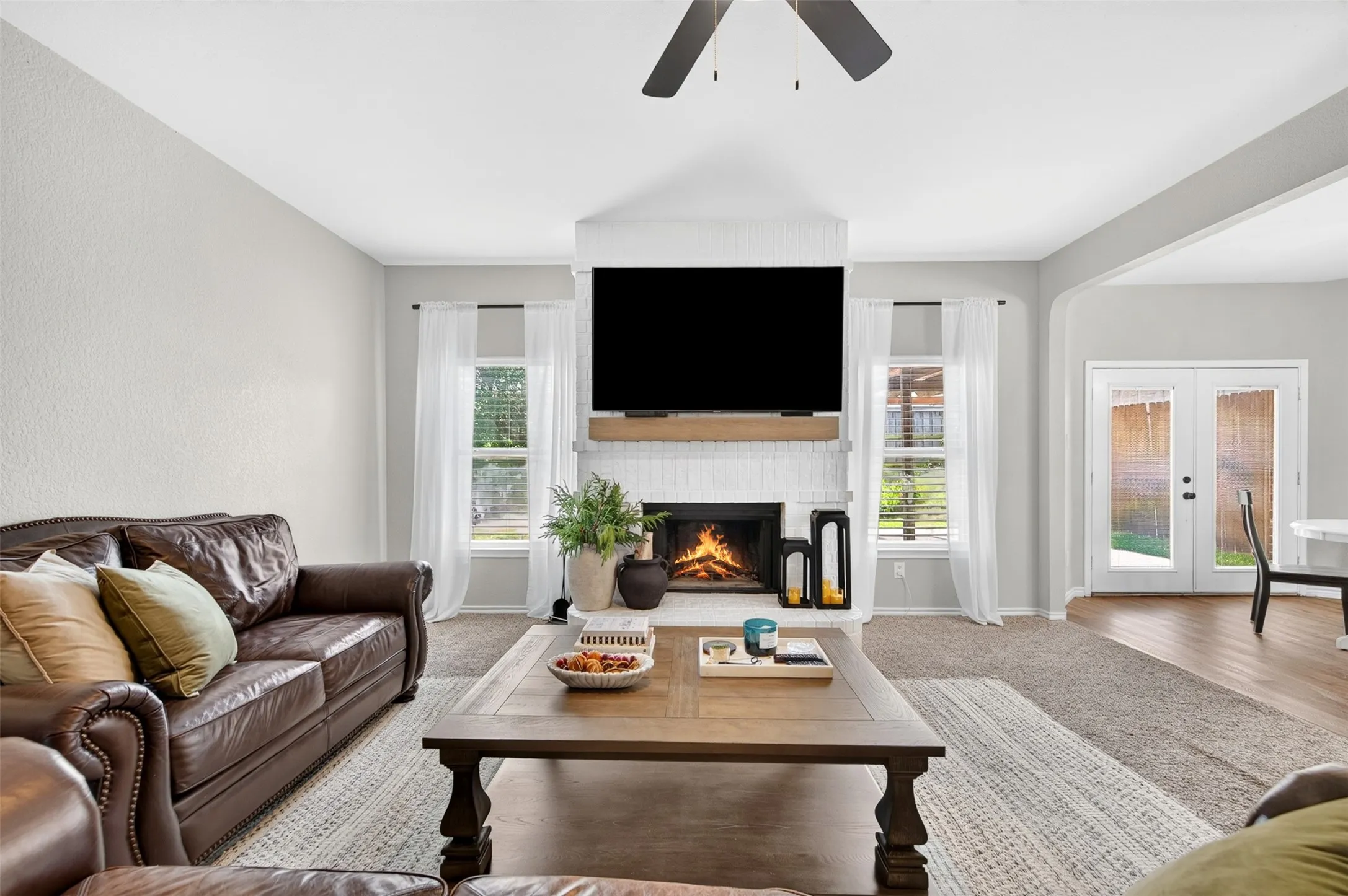 Living room featuring a white brick fireplace with a wood mantel, ceiling fan, and carpet flooring