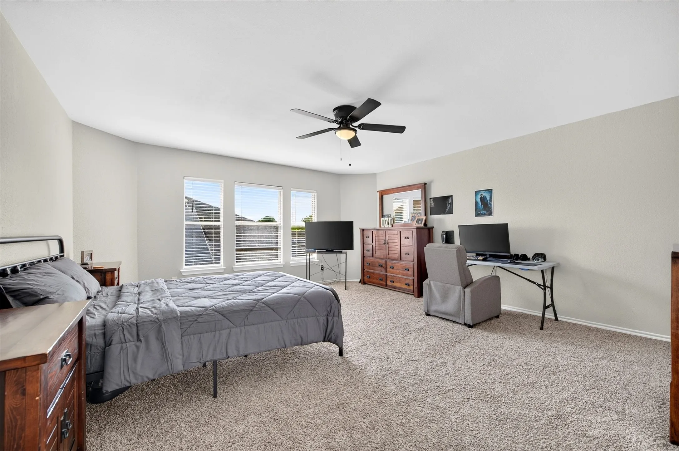 Spacious bedroom featuring neutral wall tones, plush carpeting, multiple windows providing natural light, a ceiling fan with integrated lighting, and ample floor space