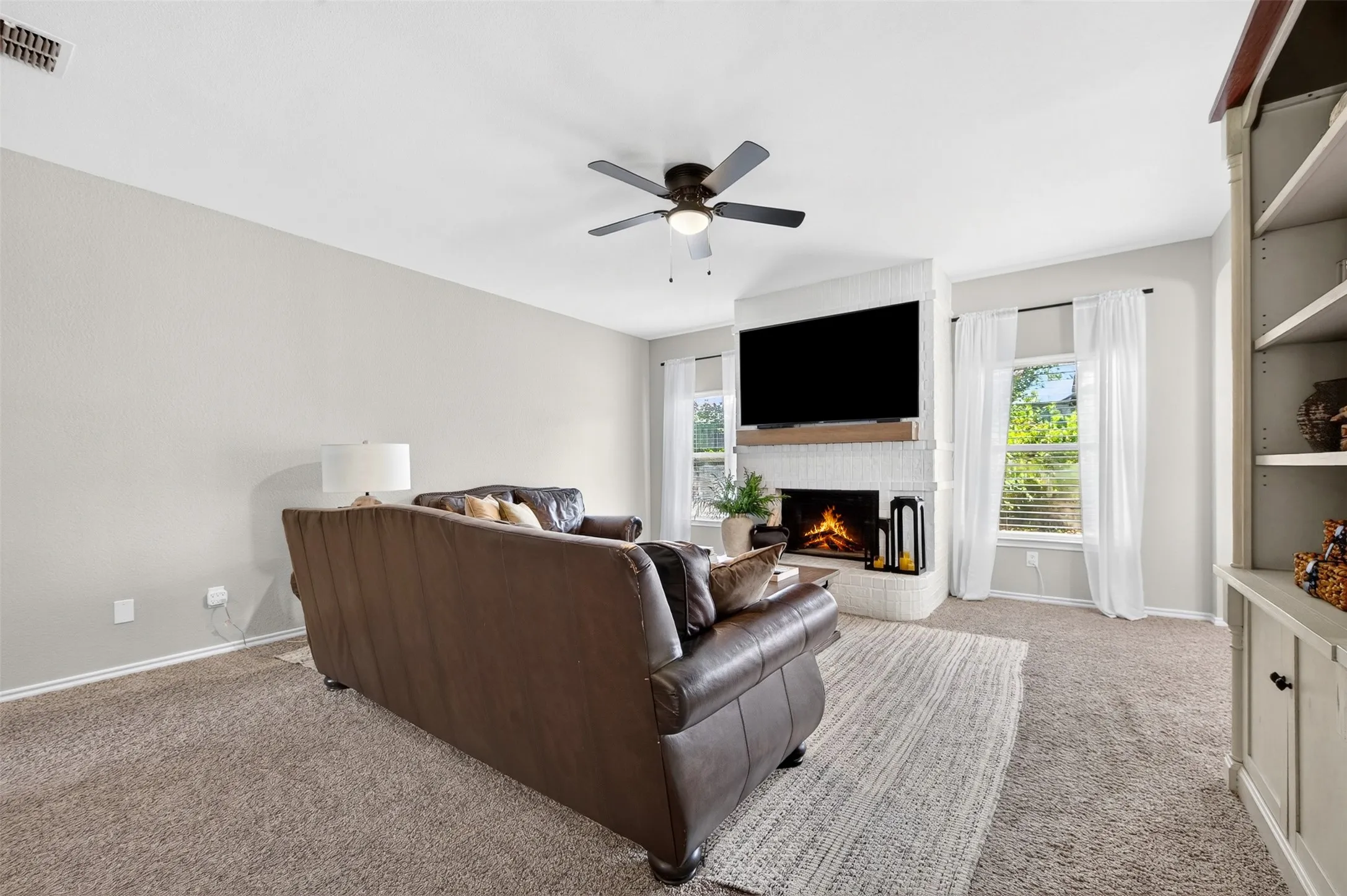 Living room featuring a white brick fireplace with a wood mantle, ceiling fan, and carpet flooring