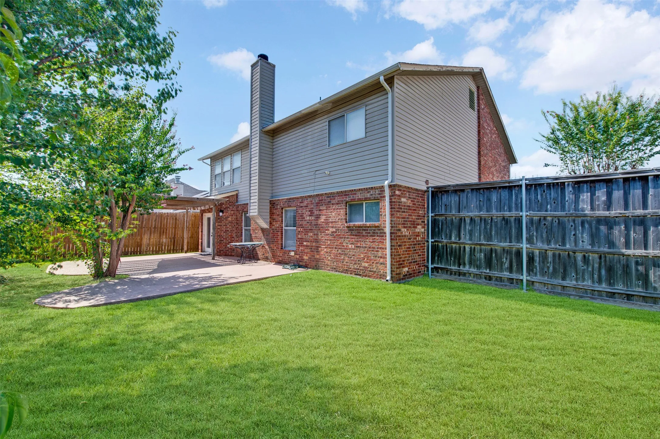 Expansive rear yard featuring a manicured lawn, a large stamped concrete patio, and mature landscaping