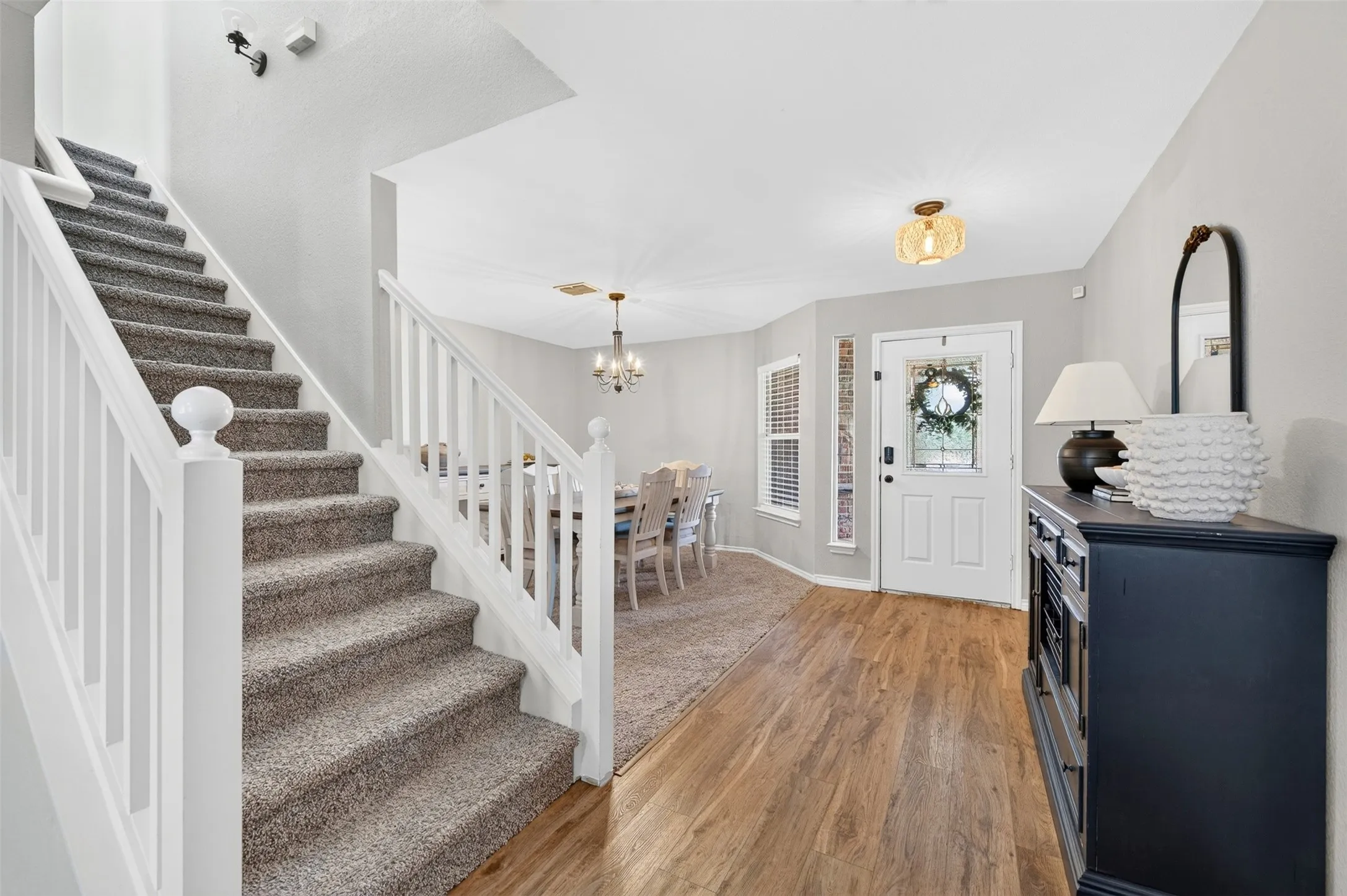 Inviting entryway featuring wood-finish flooring, a white front door with sidelights, and a staircase with white balusters and carpeted treads