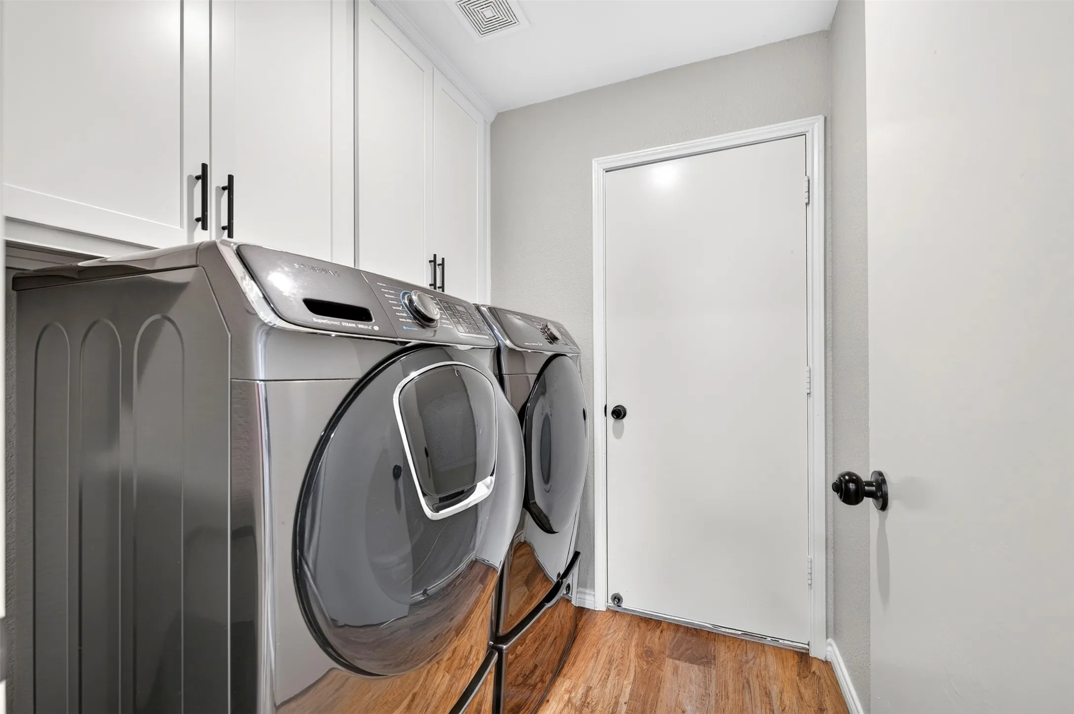 Dedicated laundry area featuring wood-finish flooring, white cabinetry with matte black hardware, and a white interior door with black hardware
