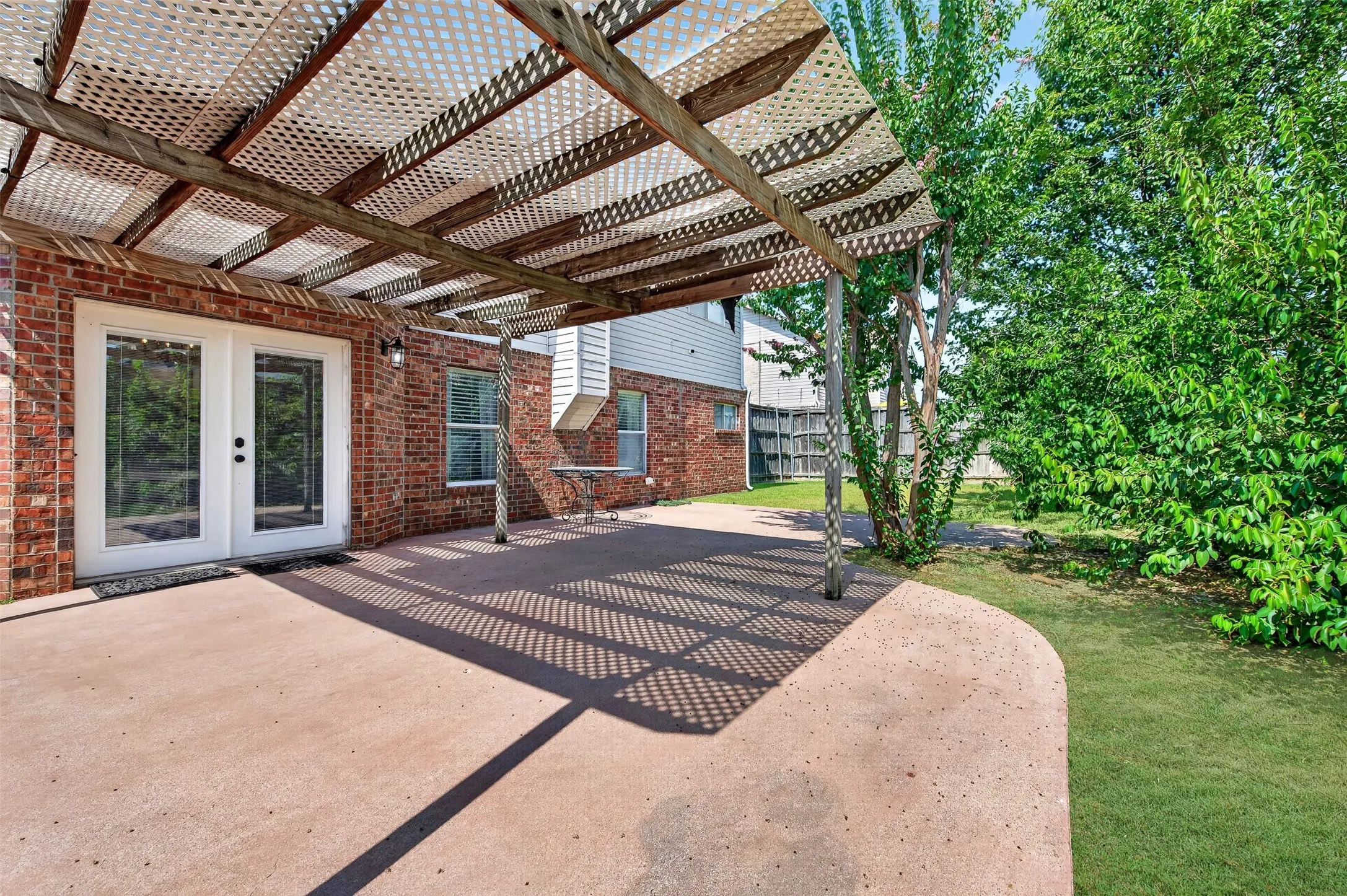 Covered patio area featuring a slatted roof structure, concrete flooring, and direct access through double glass panel doors