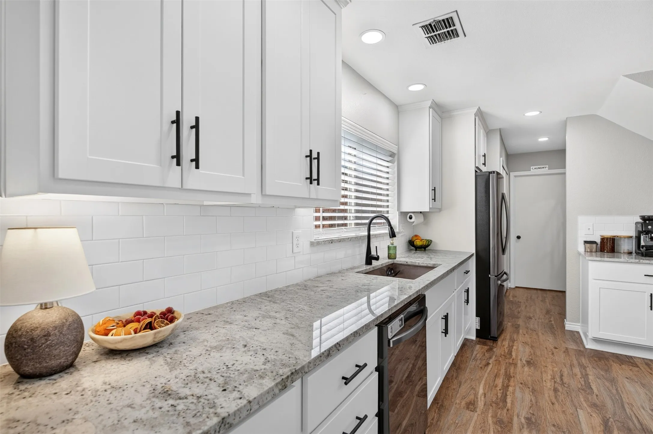Modern kitchen featuring white shaker cabinetry with black hardware, stone-finish countertops, a subway tile backsplash, stainless steel appliances, and wood-finish flooring