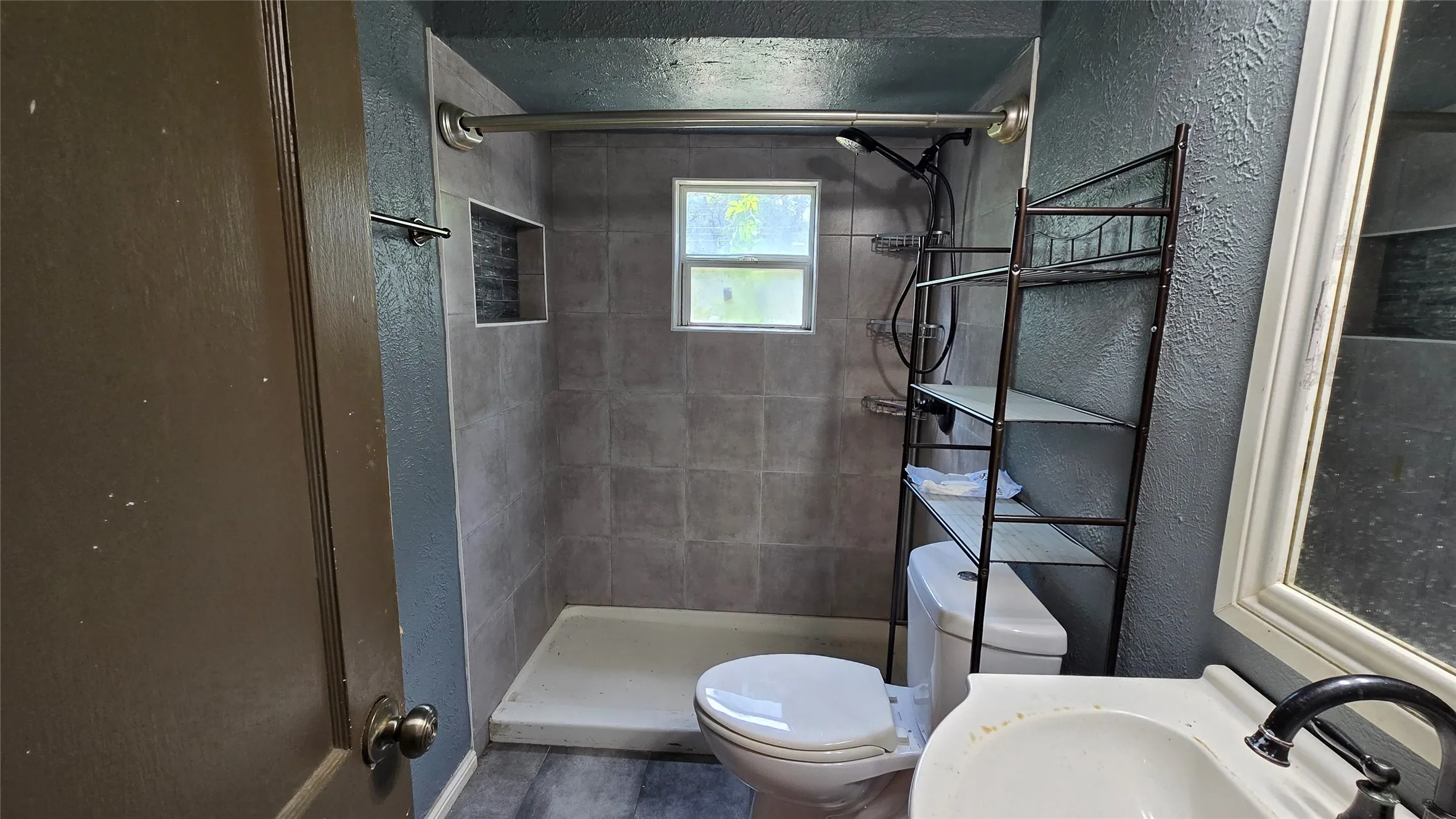 Bathroom featuring a walk-in shower with gray tile surround, a built-in shower niche, and a window