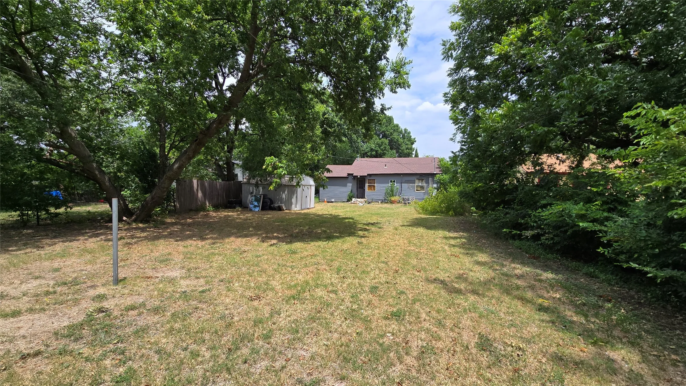 Expansive backyard framed by mature trees, featuring a detached storage shed and a privacy fence