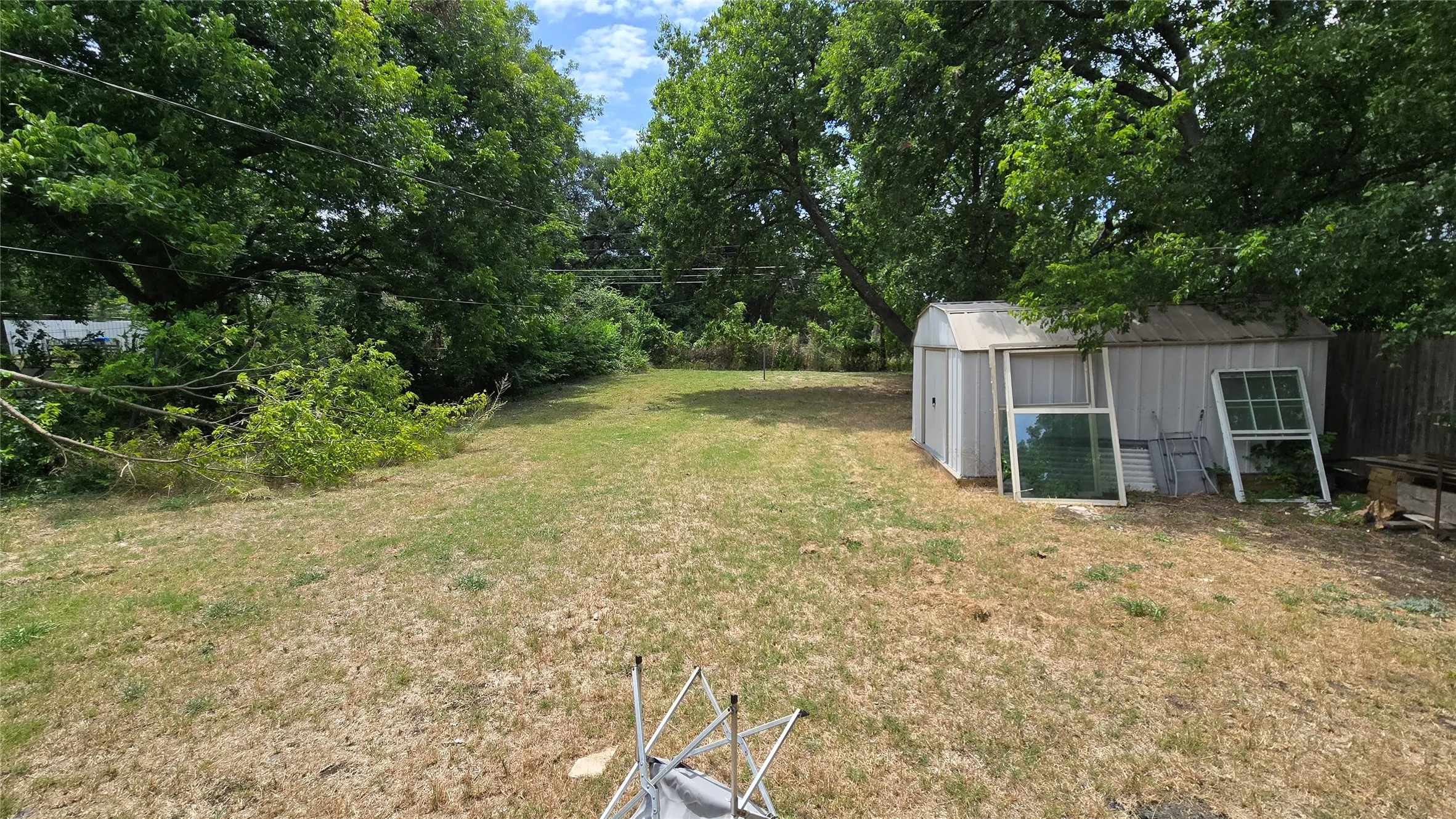 Expansive yard featuring mature trees, a metal storage shed, and a privacy fence
