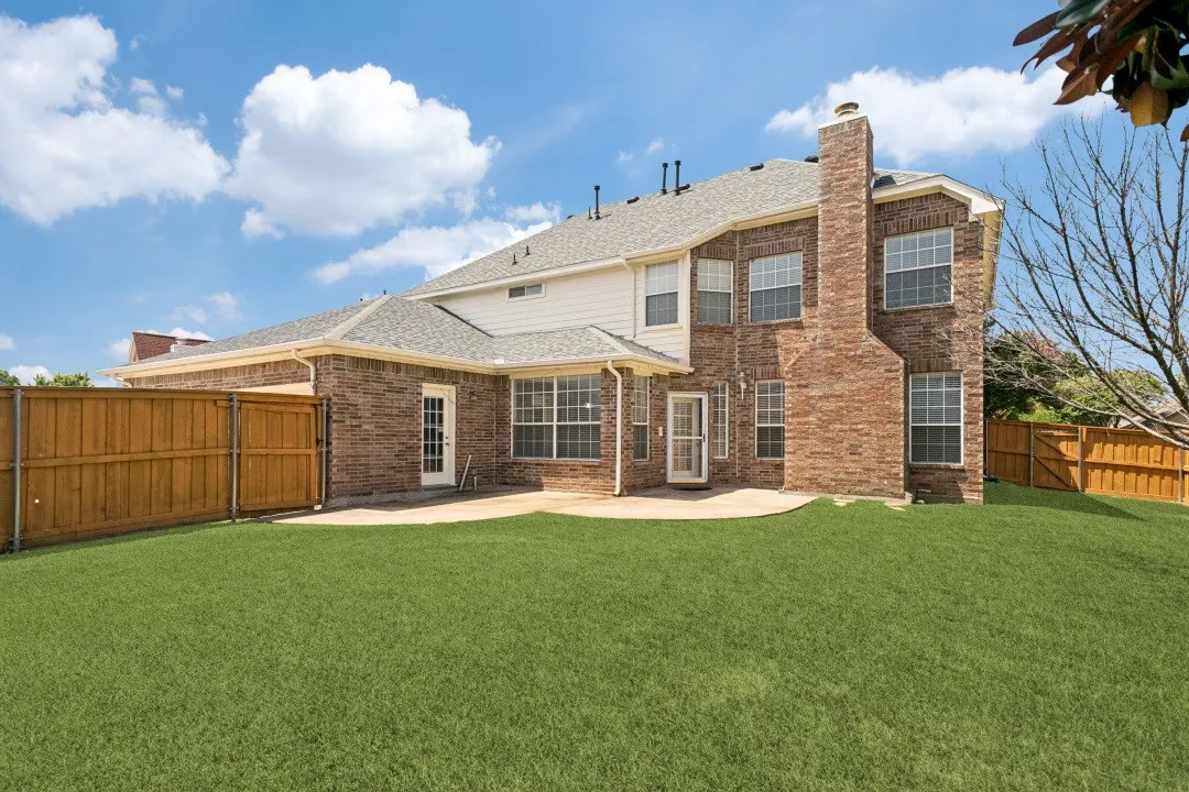 Rear exterior featuring a brick and siding facade, a large patio area, and a private fenced yard
