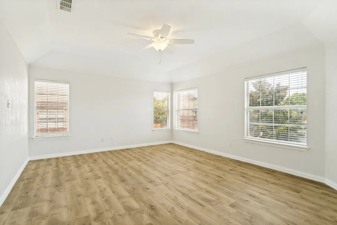 Spacious room featuring wood-finish flooring, vaulted ceiling, and a ceiling fan with light fixture