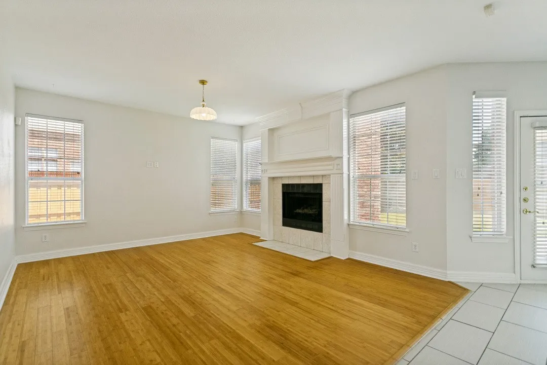 Living area featuring wood-finish flooring, a white trim fireplace with a tiled hearth, multiple windows, and a glass-paneled door