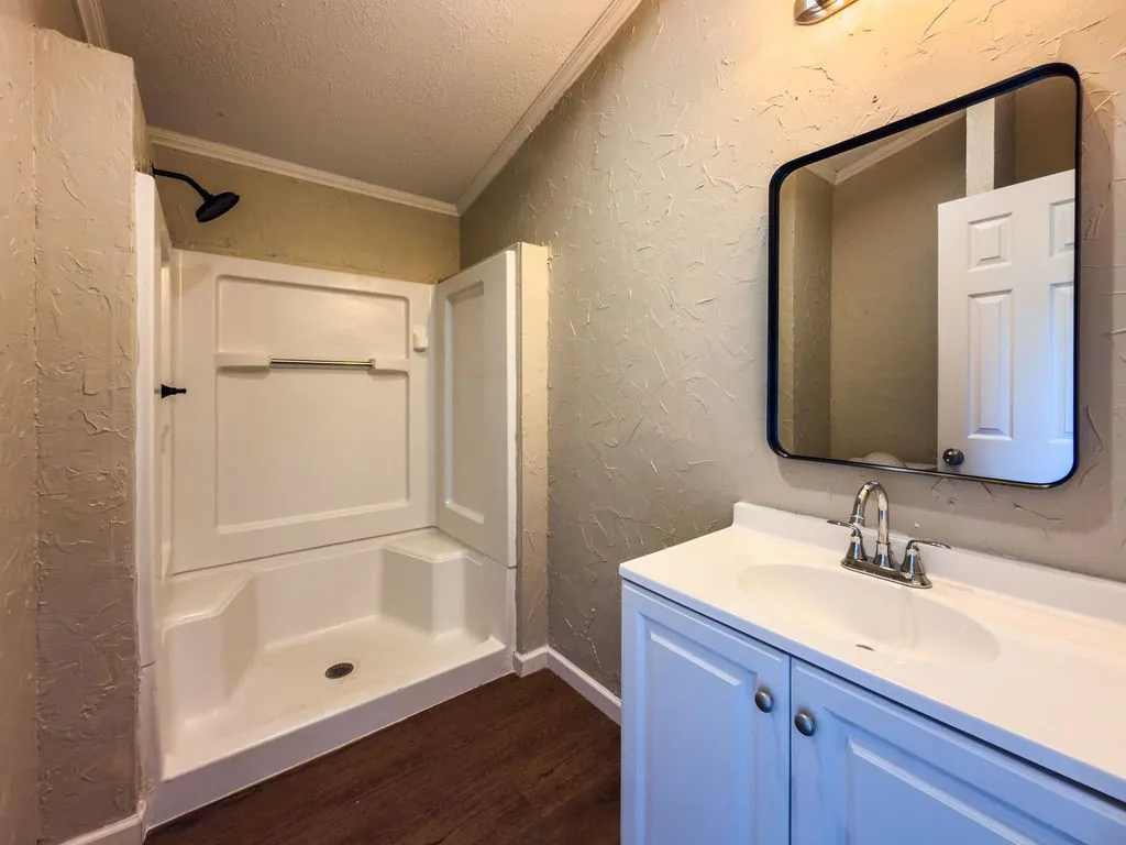 Bathroom featuring a white shower stall with a black rain showerhead, a white vanity with integrated sink, chrome faucet, and a black-framed mirror