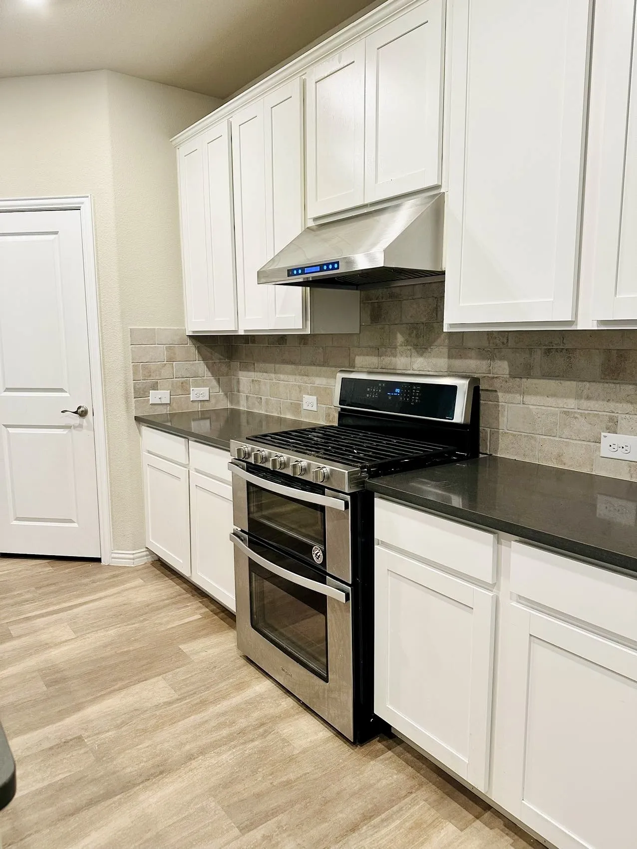 Kitchen featuring light hardwood / wood-style floors, tasteful backsplash, white cabinetry, and range with two ovens