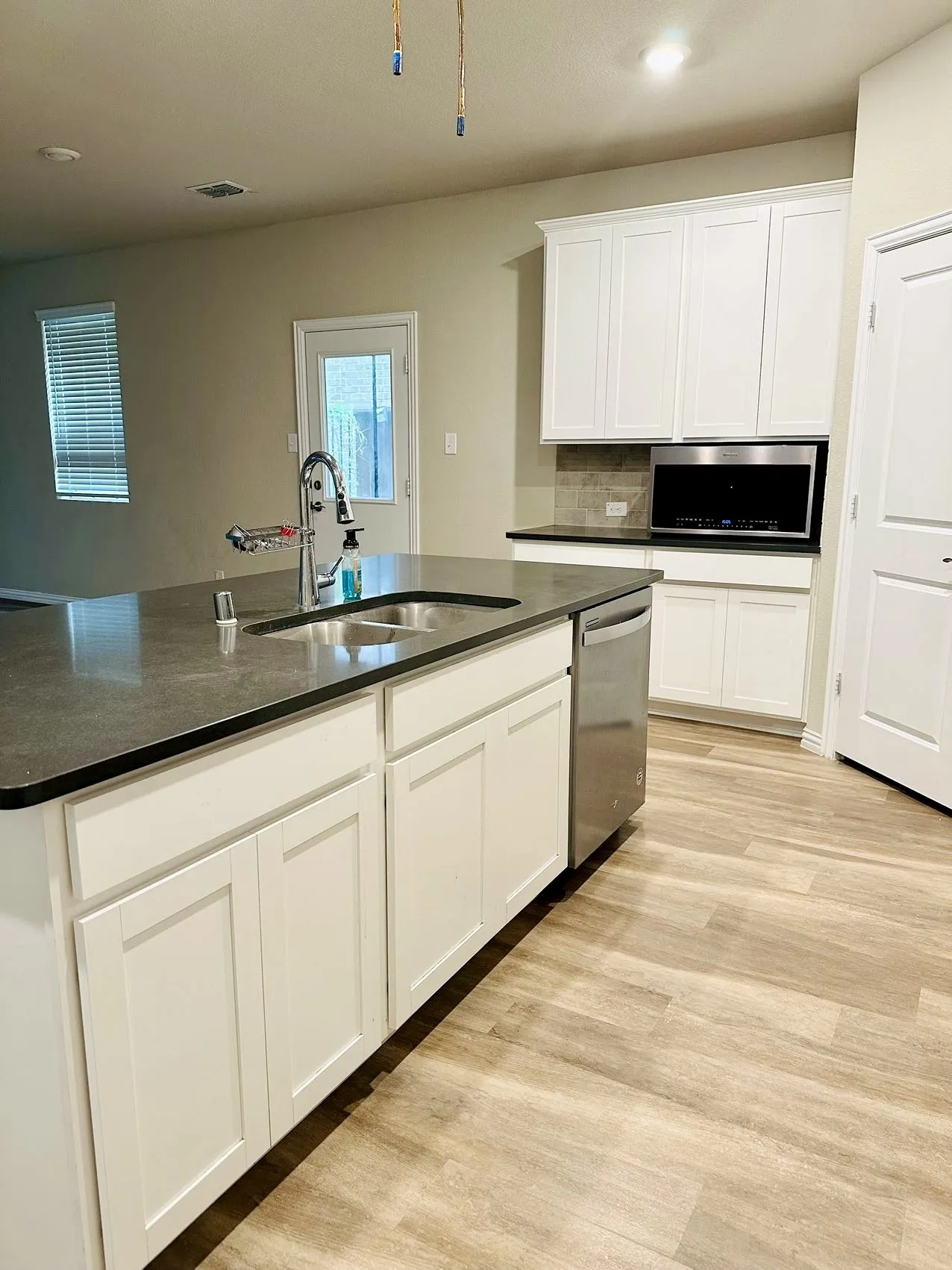 Kitchen with light hardwood / wood-style floors, stainless steel dishwasher, white cabinets, backsplash, and sink