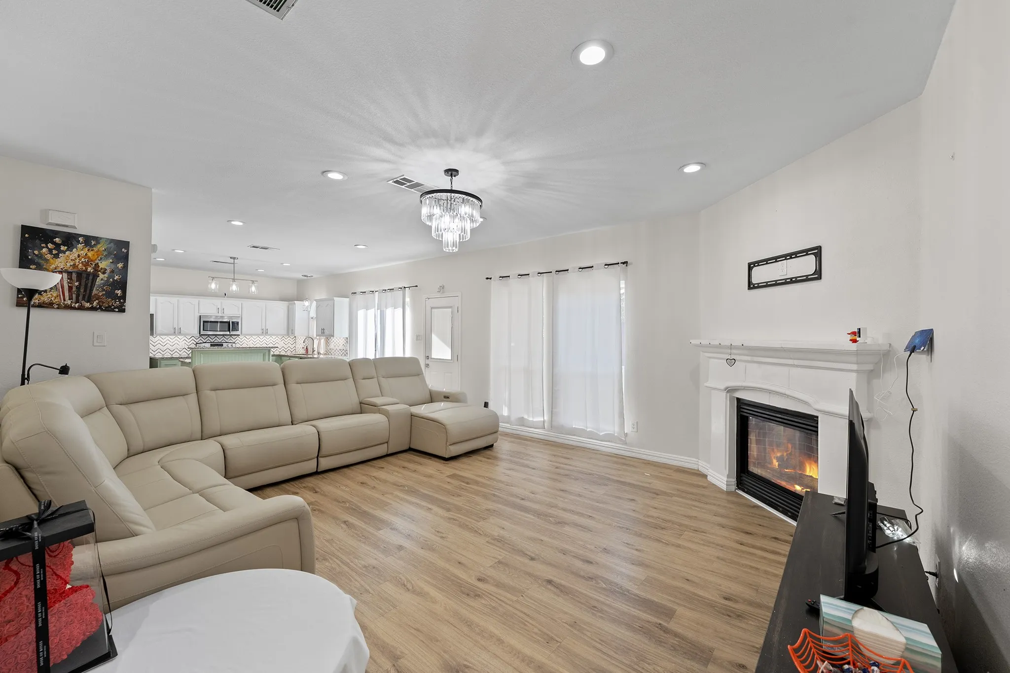 Living area featuring recessed lighting, a glass covered fireplace, light wood-type flooring, and a chandelier