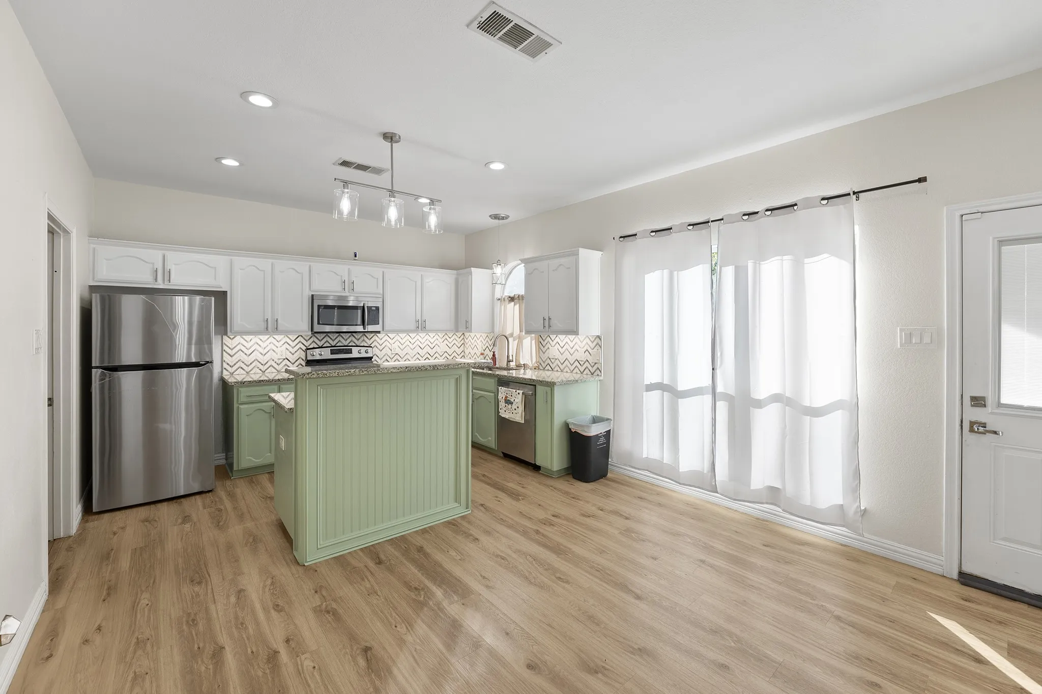 Kitchen with green cabinetry, white cabinetry, stainless steel appliances, tasteful backsplash, and a center island