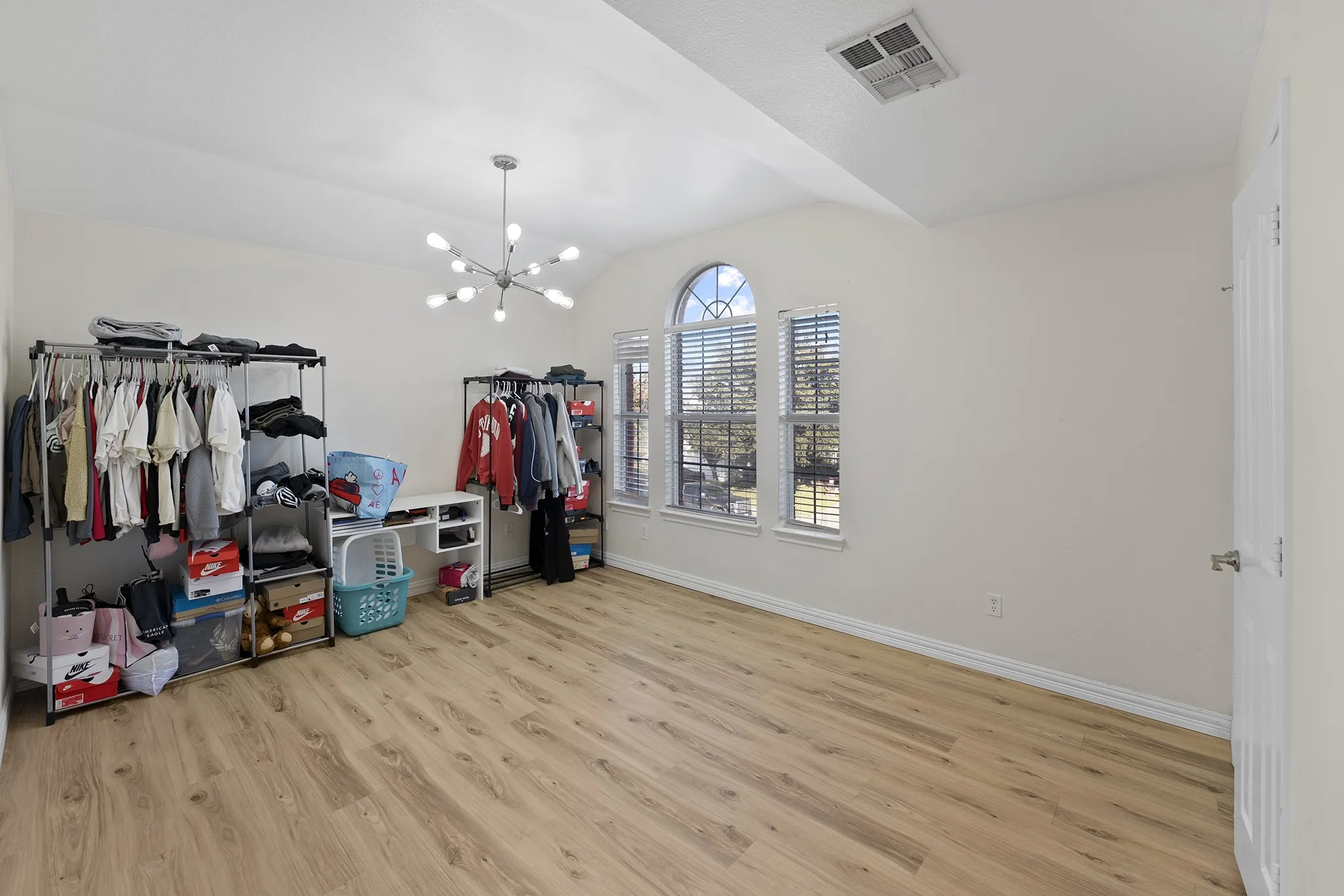 Spacious closet with light wood-type flooring, vaulted ceiling, and a chandelier