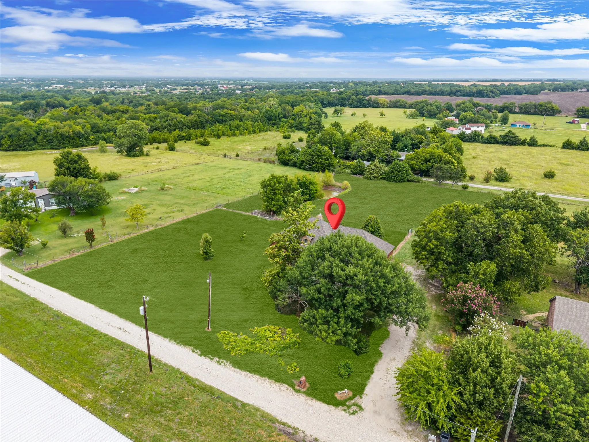 Expansive property featuring a gravel driveway, mature trees, green lawns, and a surrounding rural landscape