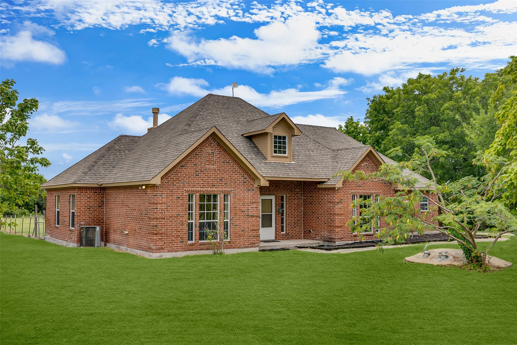 Brick exterior featuring a gabled roofline, dormer window, and mature landscaping