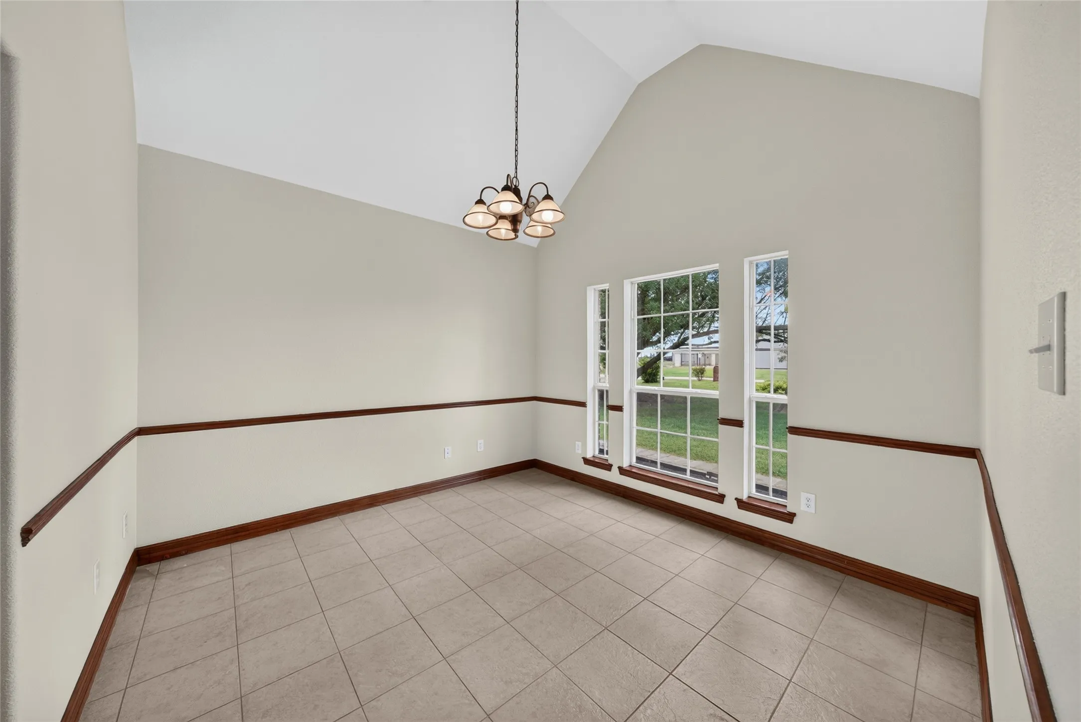 Vaulted ceiling room featuring tiled flooring, decorative chair rail molding, and three large windows with grid patterns