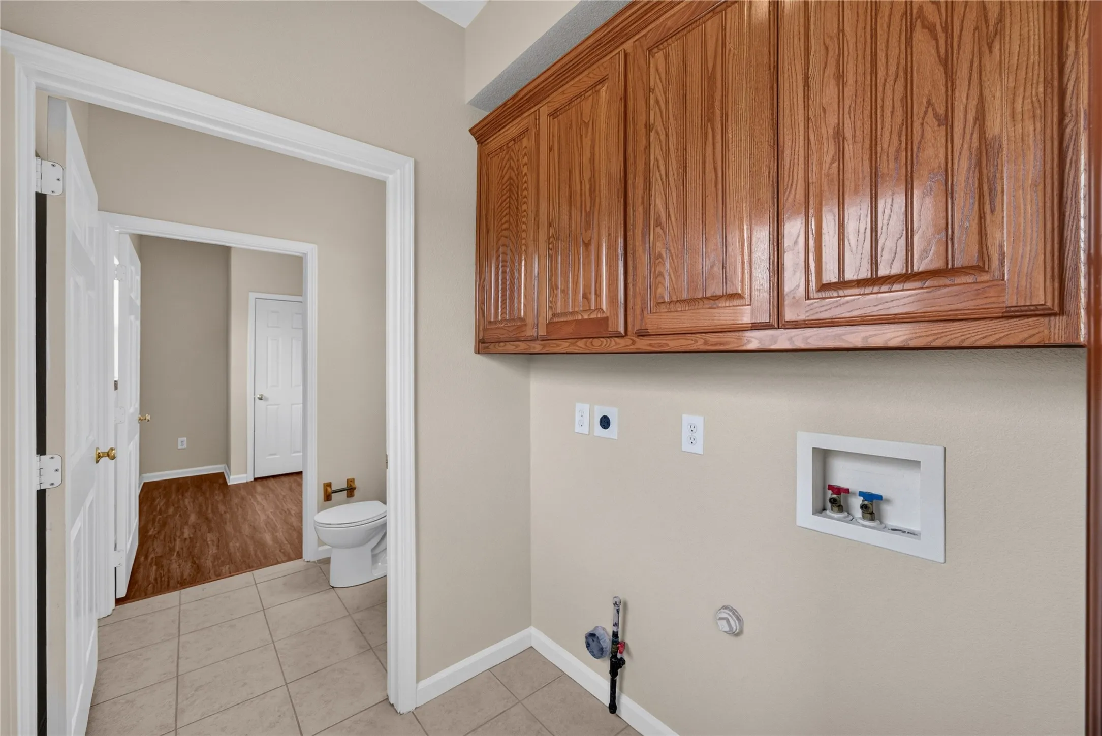 Utility area with wood-finish cabinetry, neutral wall paint, and tiled flooring