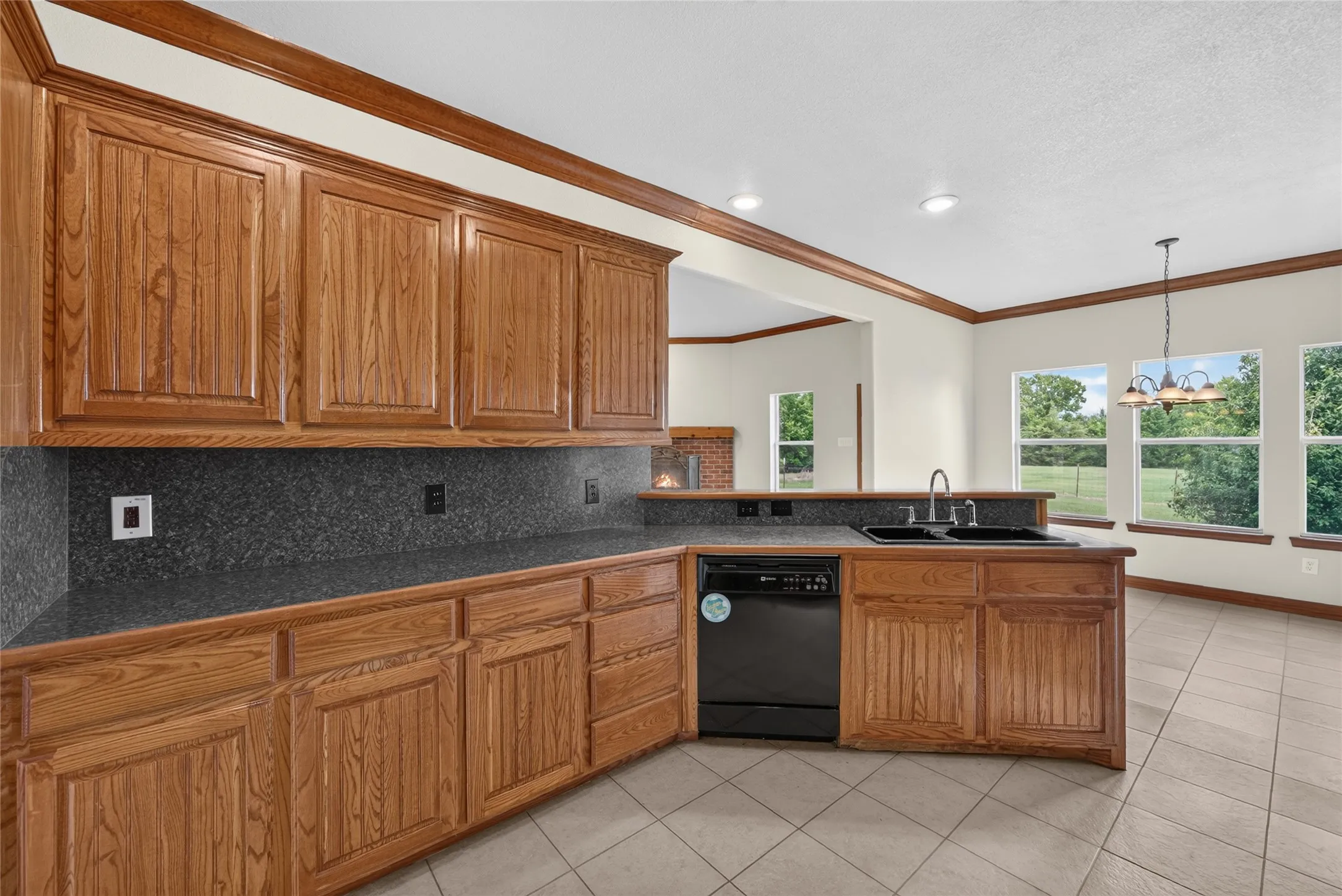 Kitchen featuring wood cabinetry, dark countertops, built-in dishwasher, and a double basin sink