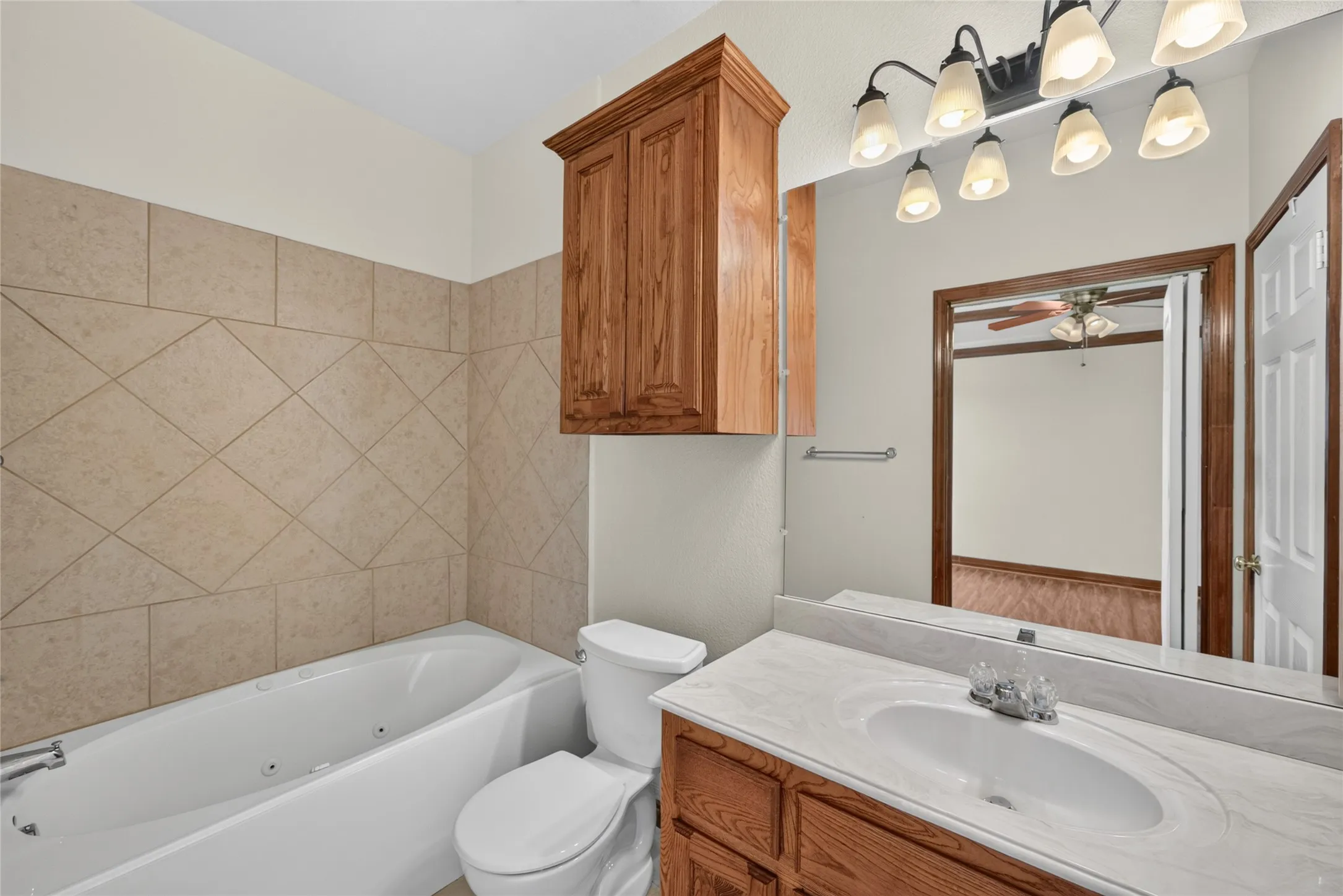 Bathroom featuring a white jetted tub, ceramic tile surround, and a toilet
