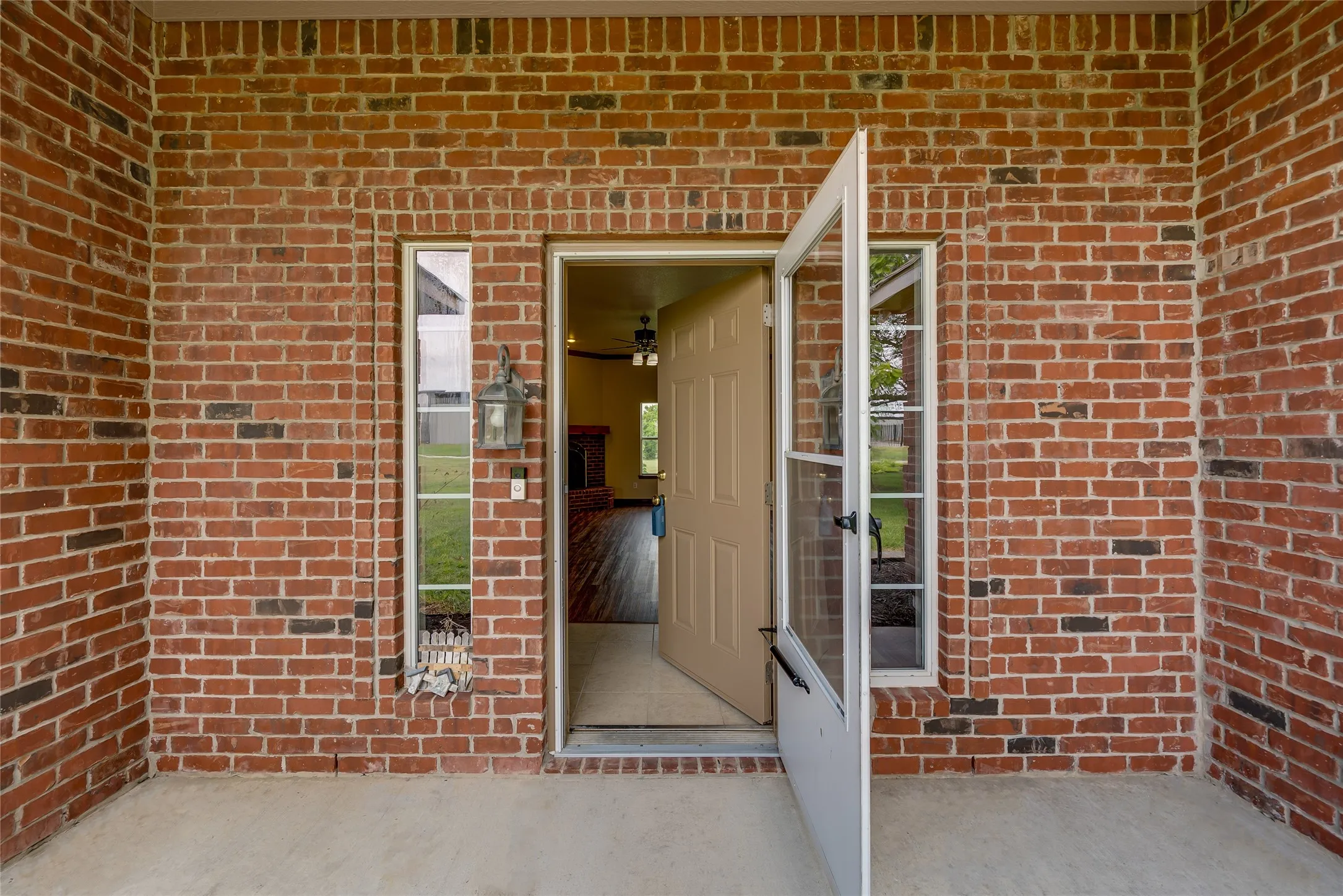 Brick exterior with a covered porch, featuring a tan entry door with a screen door, and vertical window accents