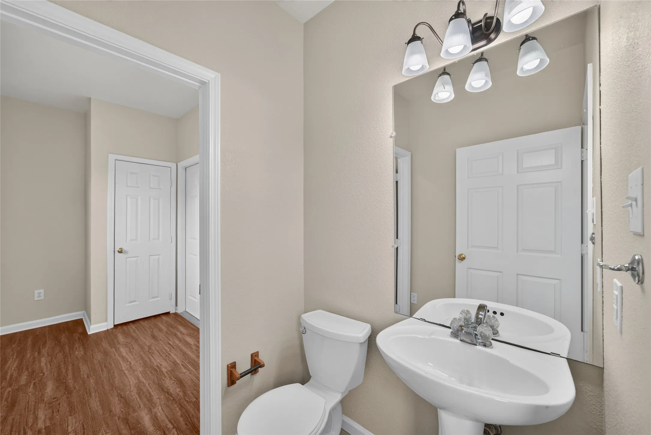 Bathroom featuring a pedestal sink with chrome faucet, a standard toilet, and a five-light vanity fixture