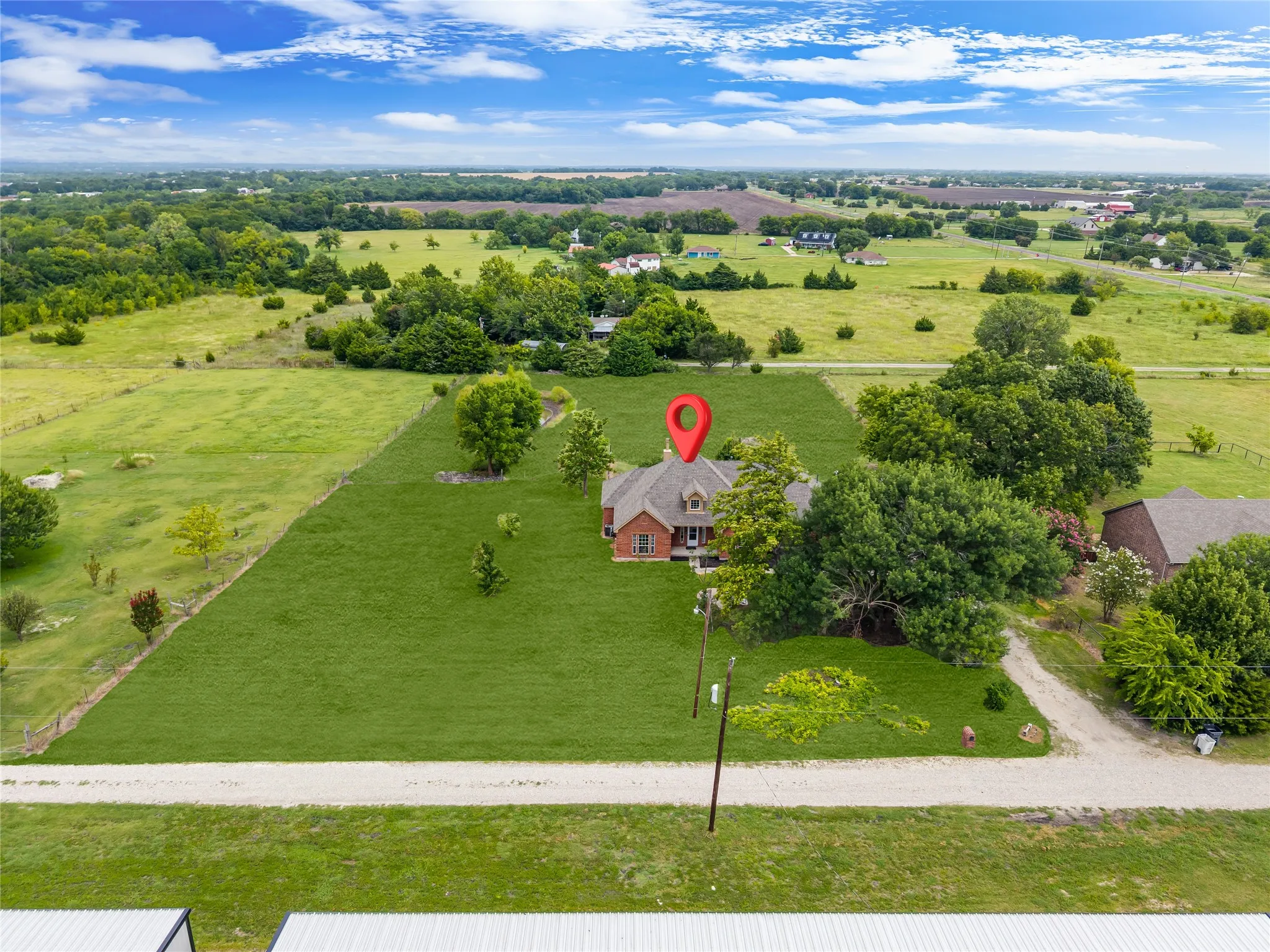 Expansive green landscape surrounding a brick residence with a dormer and mature trees