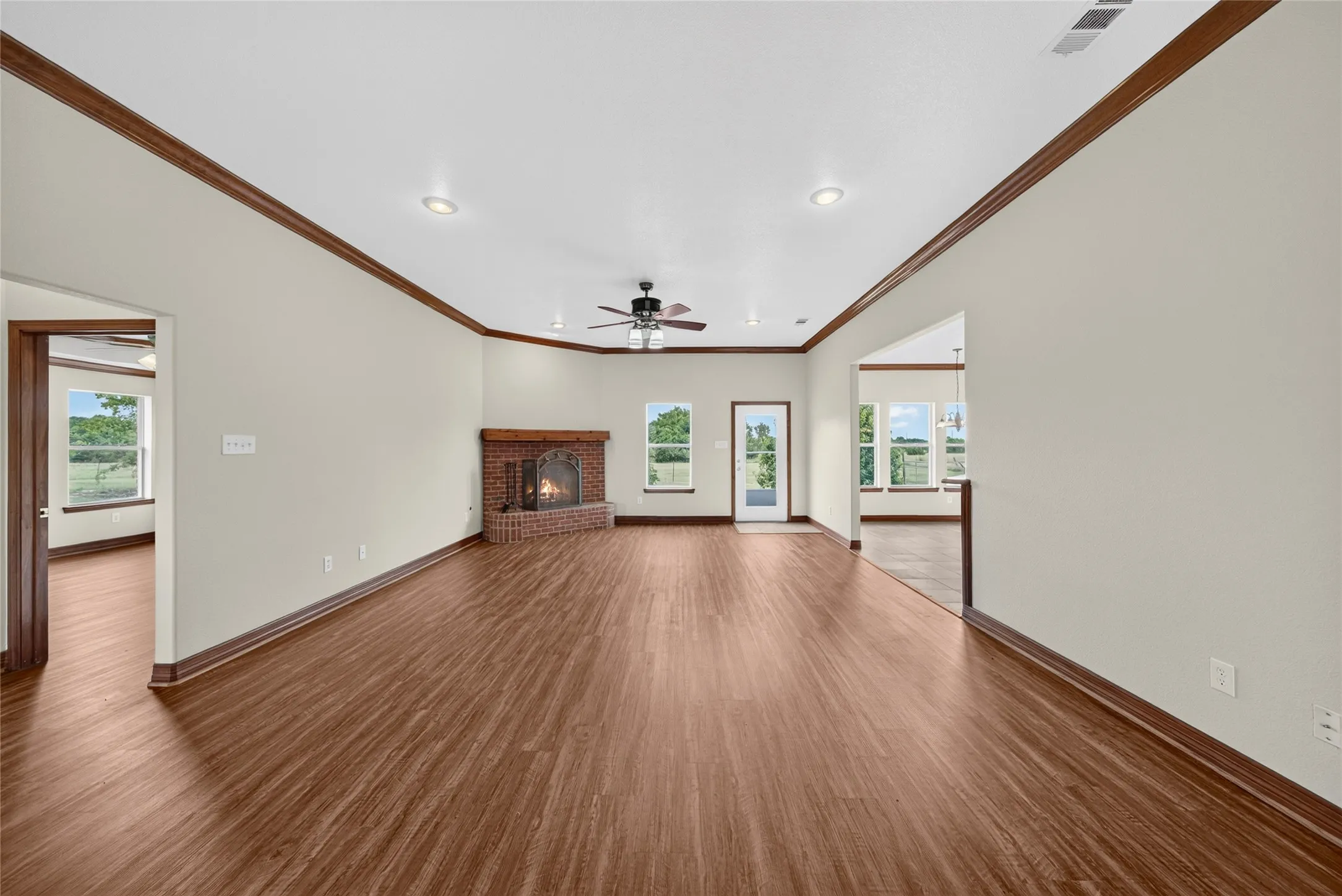 Spacious interior featuring wood-finish flooring throughout, a brick fireplace with a hearth, multiple windows, recessed lighting, and a ceiling fan