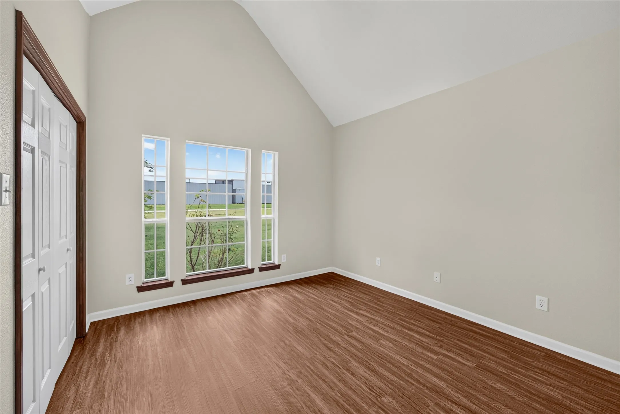 Vaulted ceiling room featuring wood-finish flooring, light neutral wall paint, and white trim