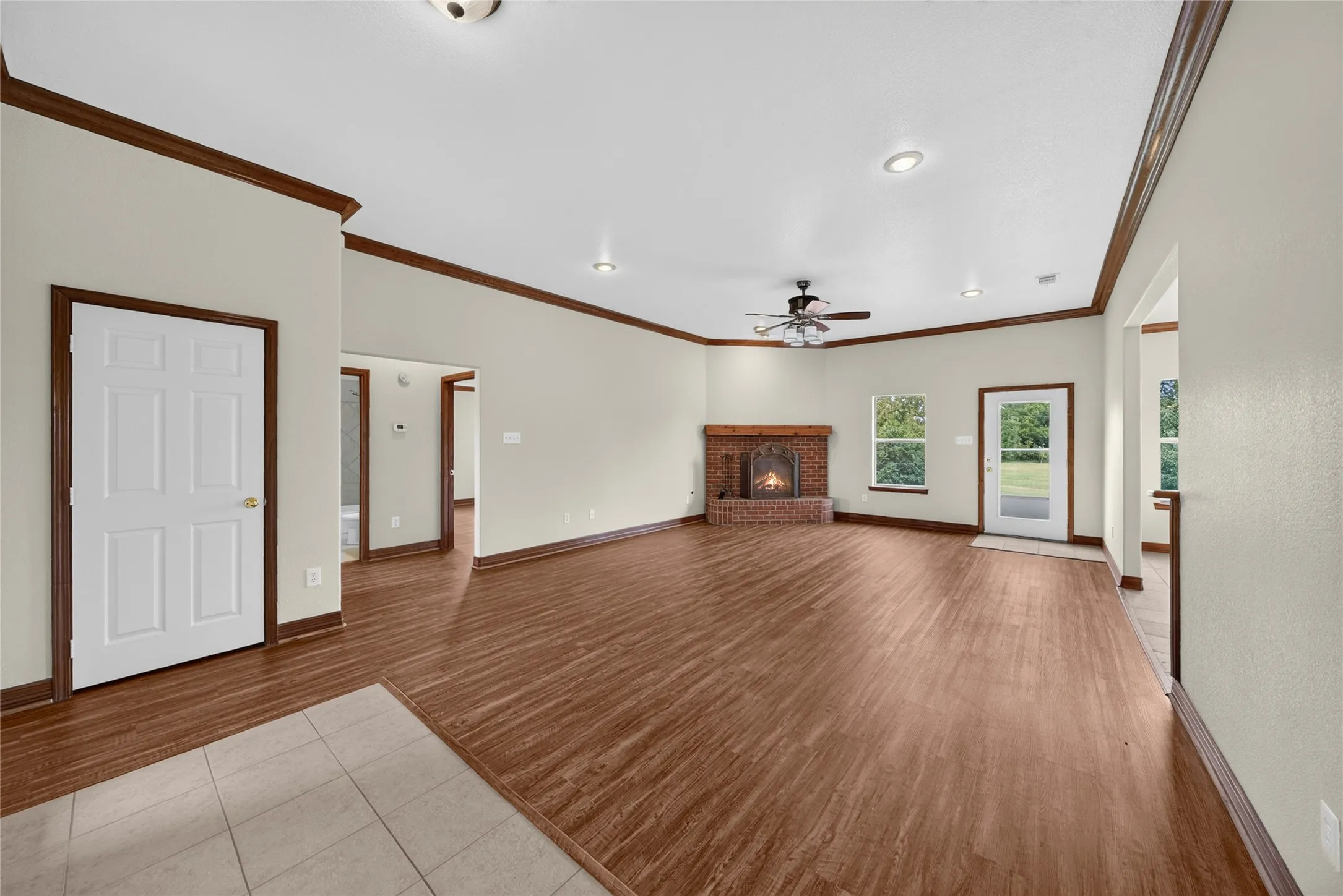 Spacious living area featuring wood-finish flooring, a brick fireplace, recessed lighting, a ceiling fan, and crown molding accents