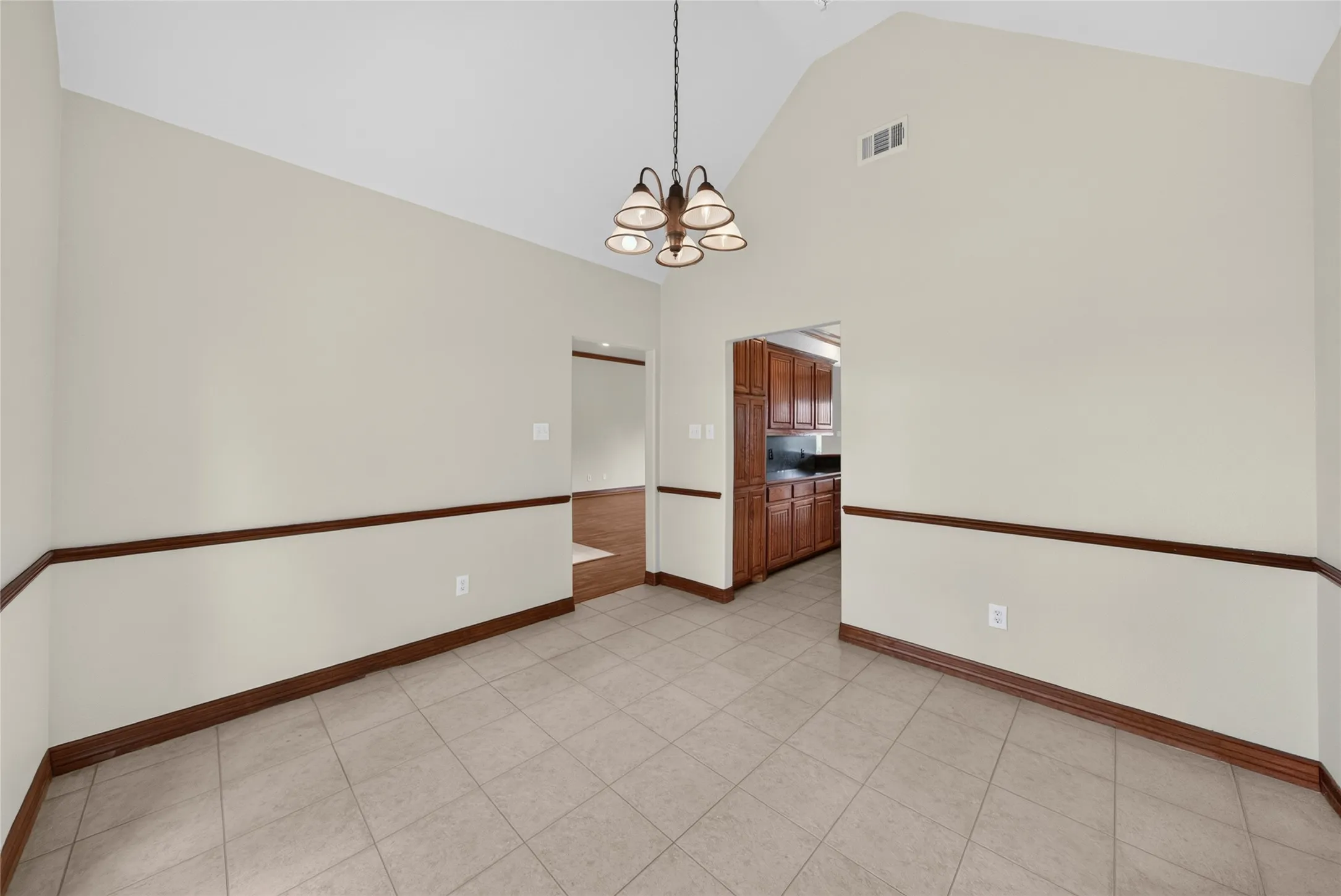 Vaulted ceiling dining area featuring neutral wall tones, decorative chair rail molding, and tile flooring