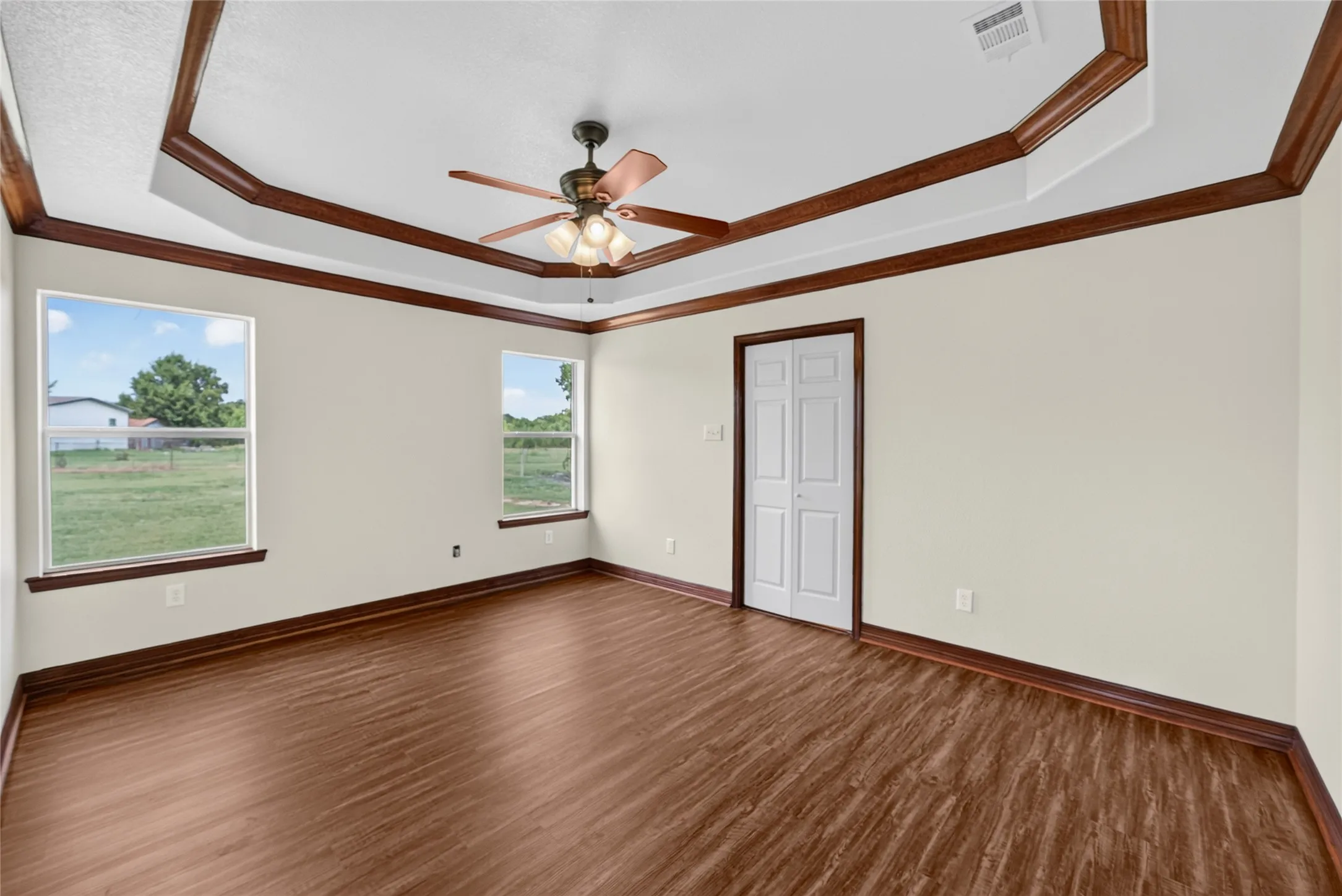 Spacious room featuring wood-finish flooring, light-toned walls, and a tray ceiling with decorative wood trim