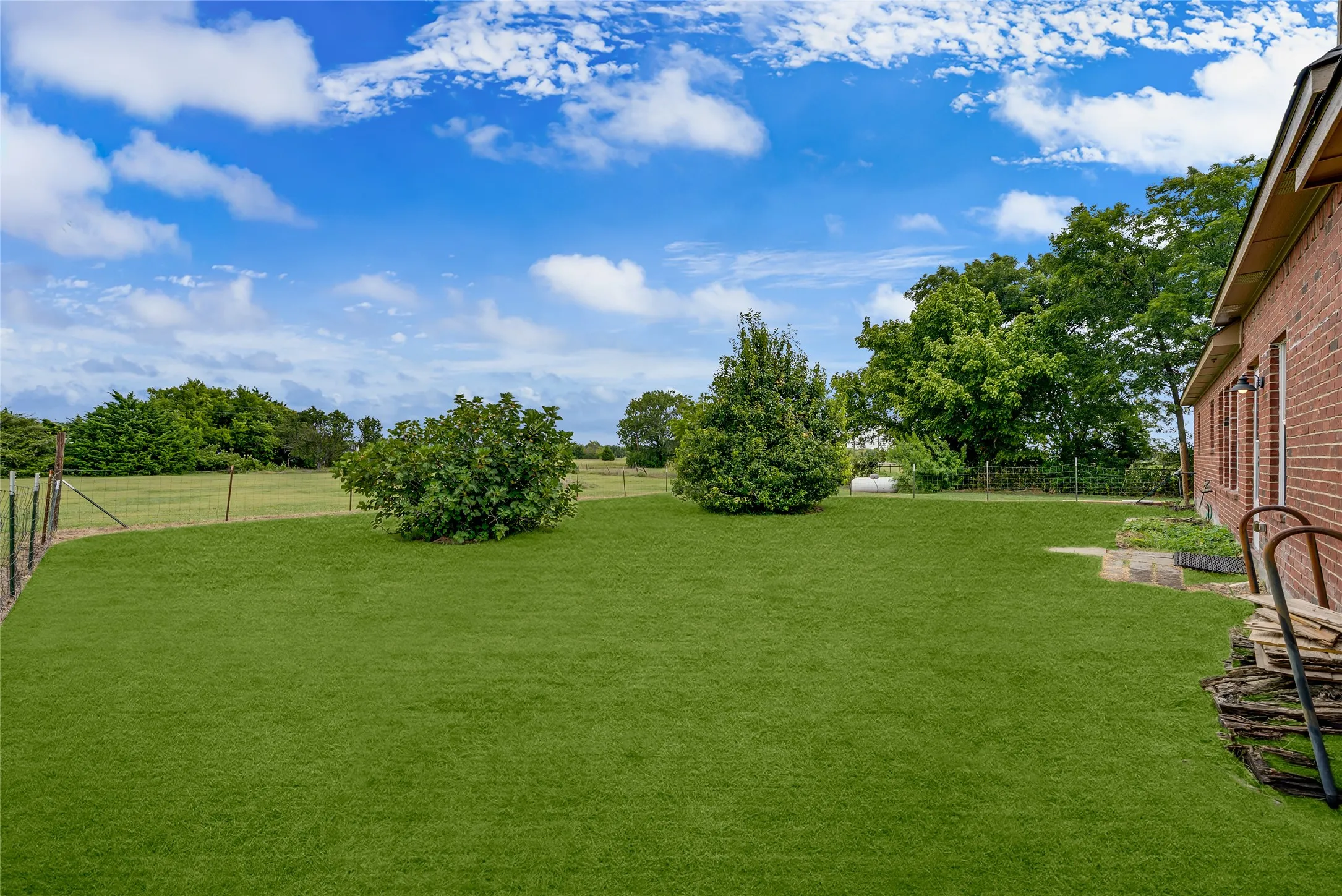 Expansive green lawn with mature landscaping and a partial brick exterior