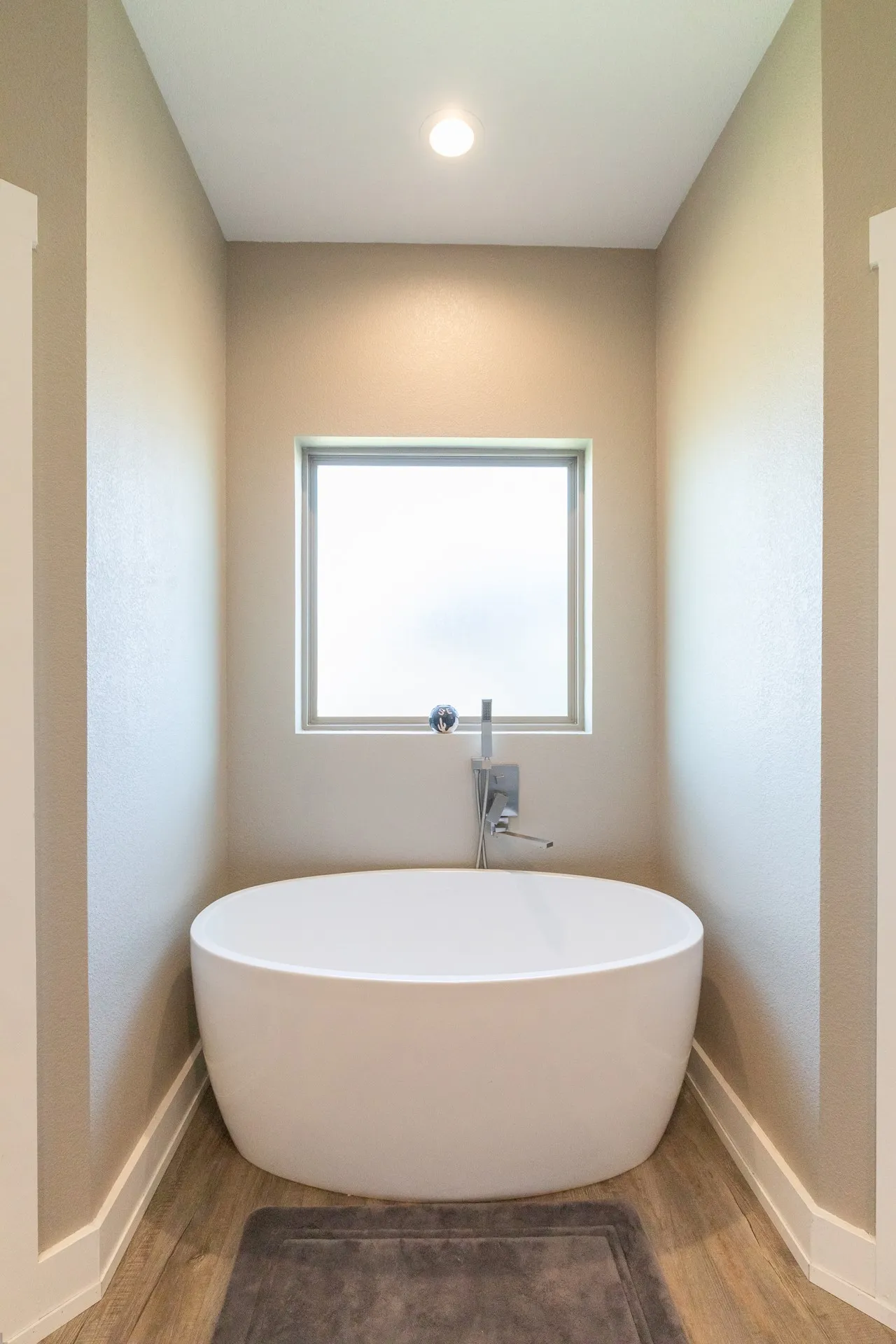 Freestanding soaking tub with a wall-mounted faucet, privacy window, recessed lighting, and wood-finish flooring