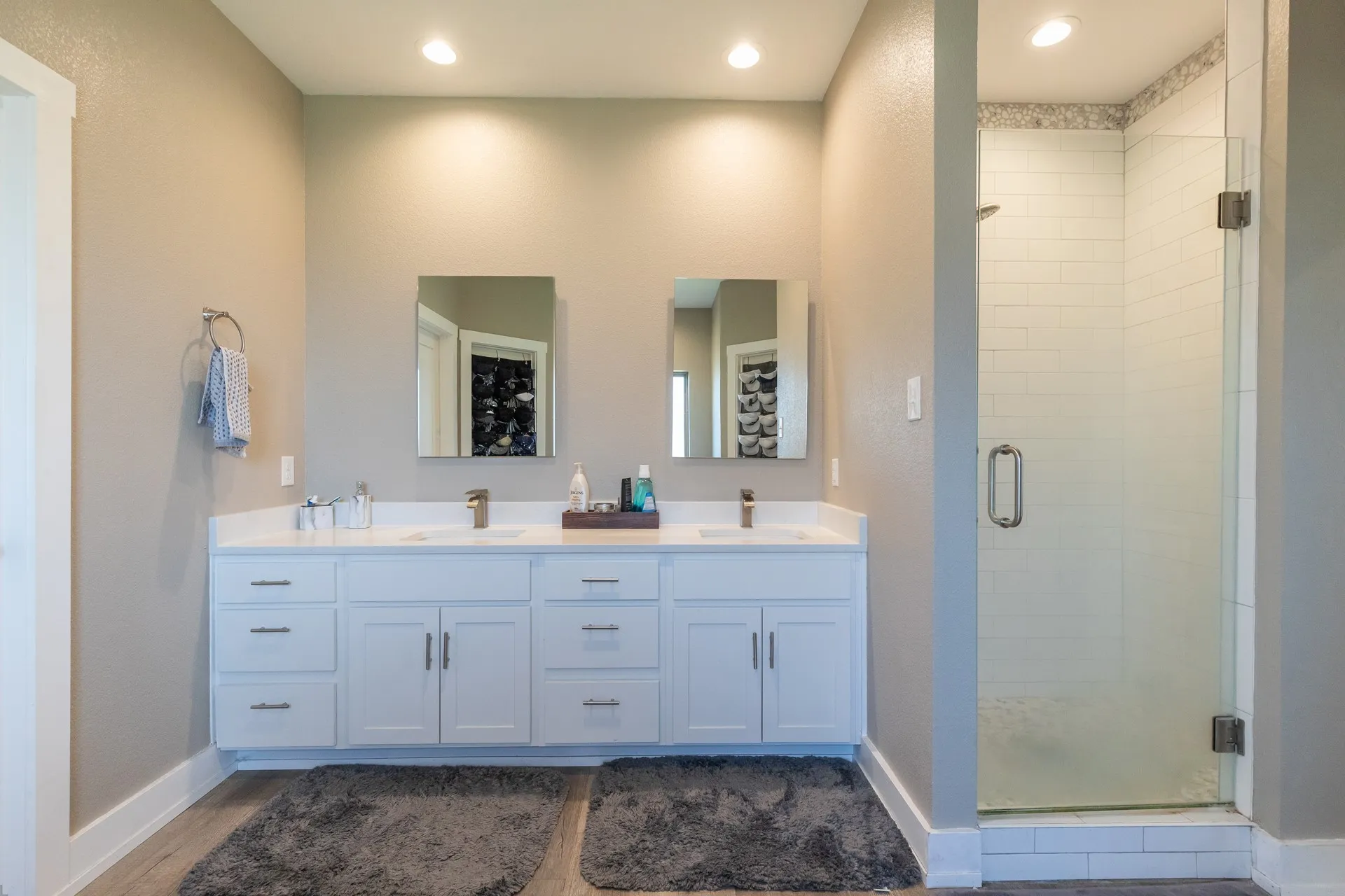 Bathroom featuring a dual vanity with white cabinetry and undermount sinks, flanked by a glass-enclosed shower with subway tile