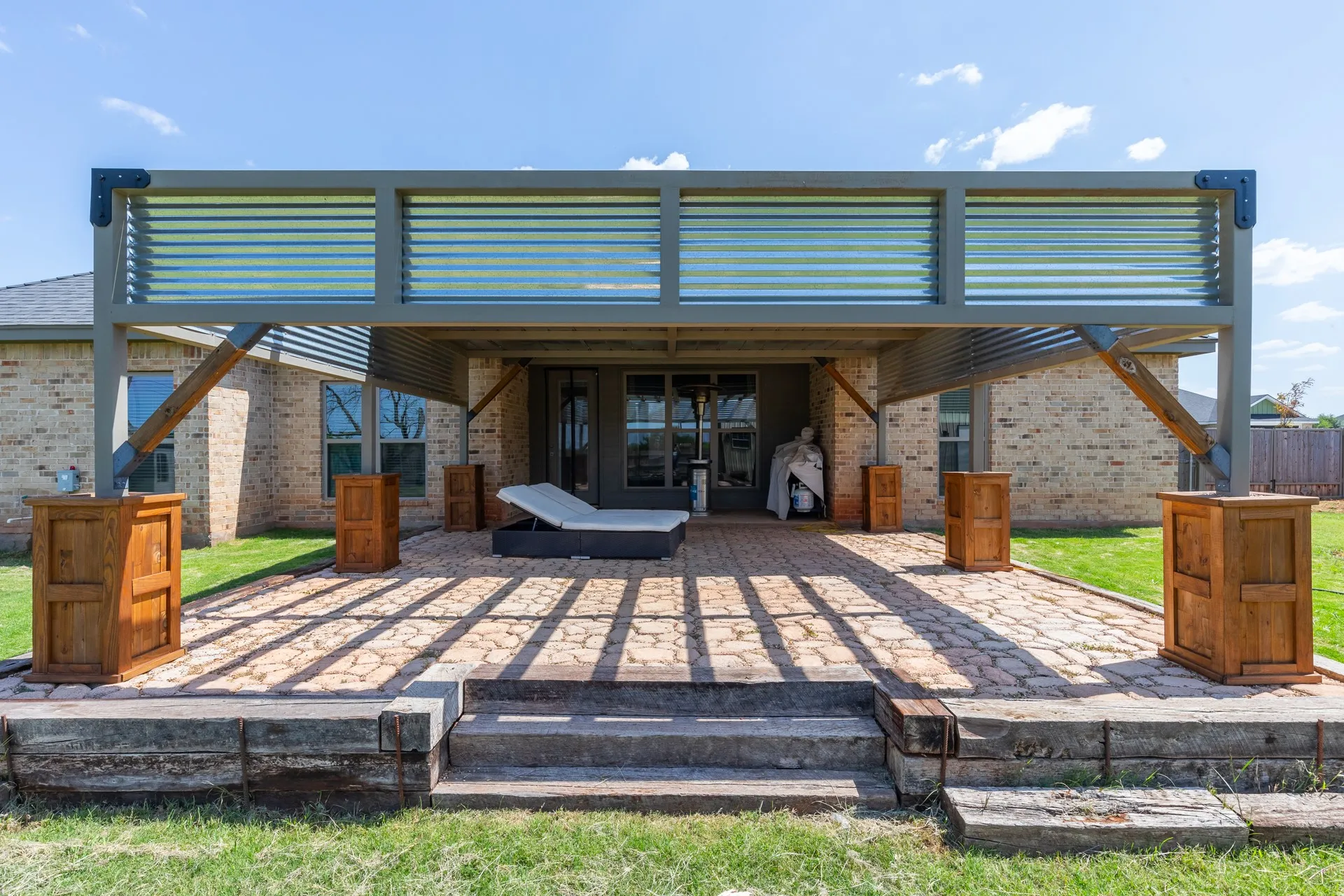 Expansive brick paver patio featuring a modern pergola with corrugated paneling