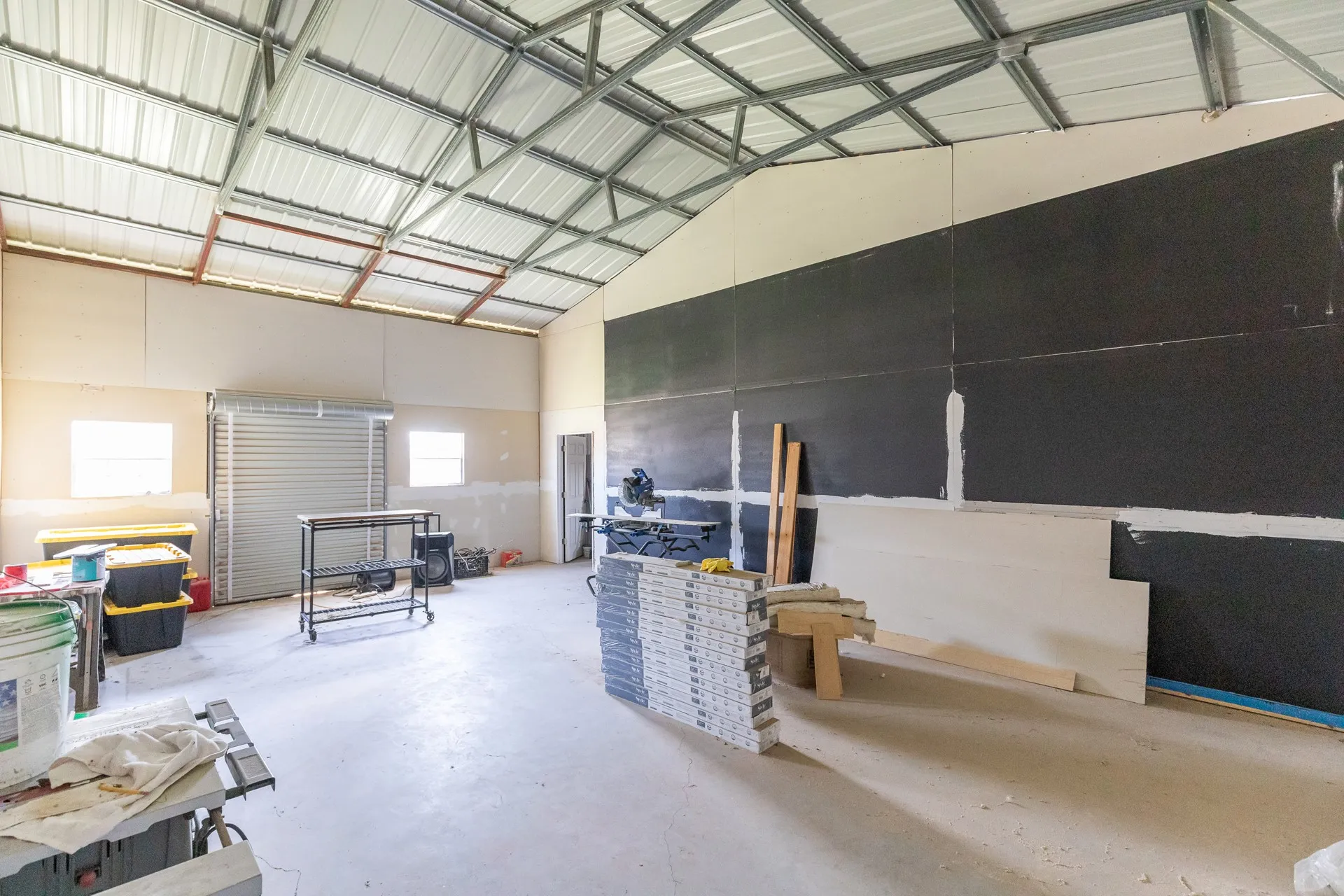 Spacious interior featuring a high vaulted metal ceiling, concrete flooring, and a large roll-up door