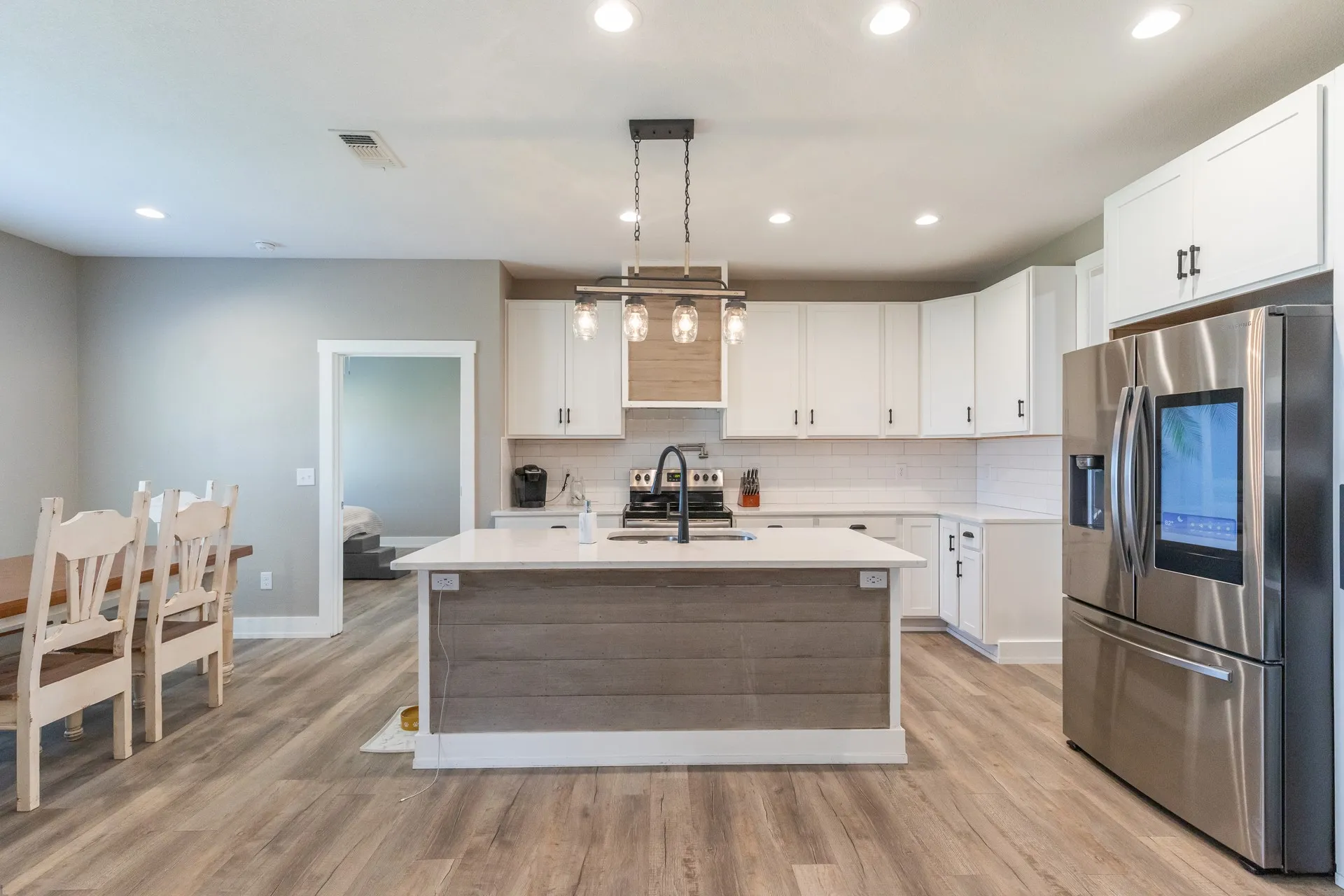 Modern kitchen featuring an island with wood-finish paneling, white shaker cabinetry, stainless steel appliances, and wood-finish flooring