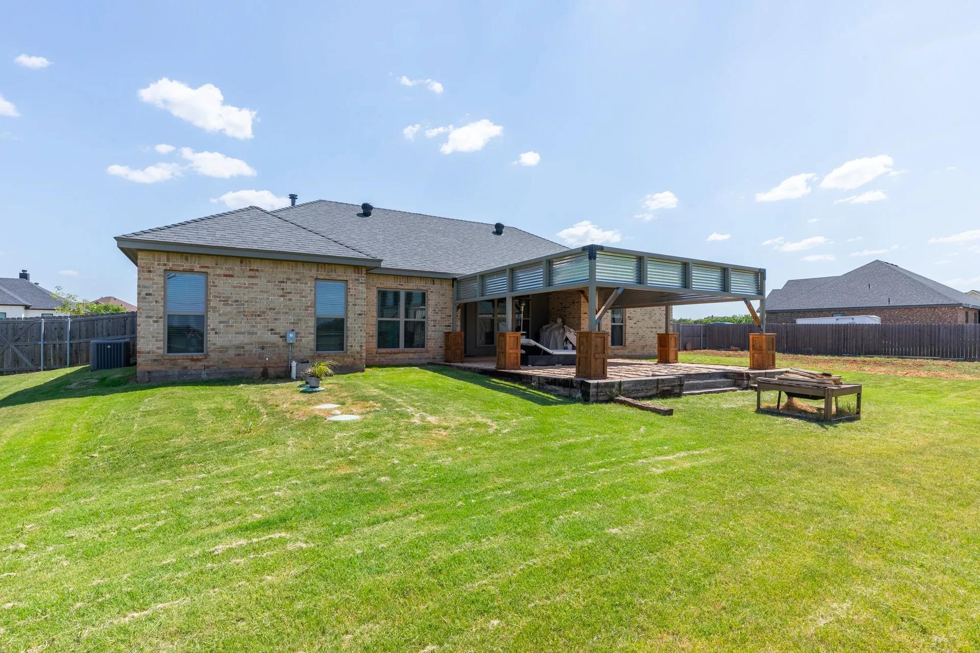 Expansive backyard featuring a covered patio with corrugated metal accents, large wood support beams, and a multi-level wood deck